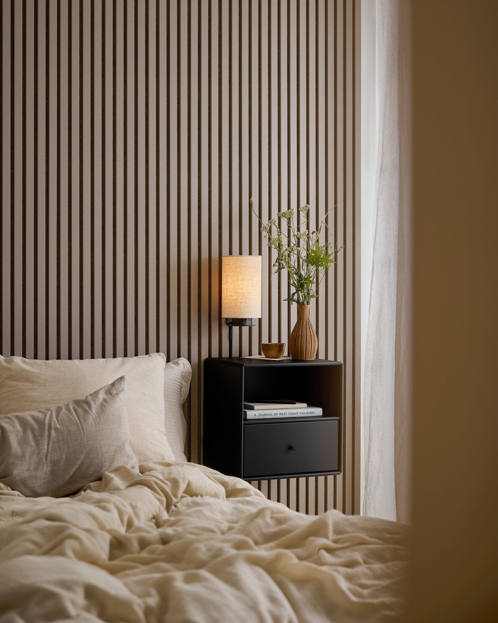 Łóżko z kremową pościelą obok czarnej szafki nocnej, na tle ściany z paneli Akupanel w kolorze Dark Cashmere.