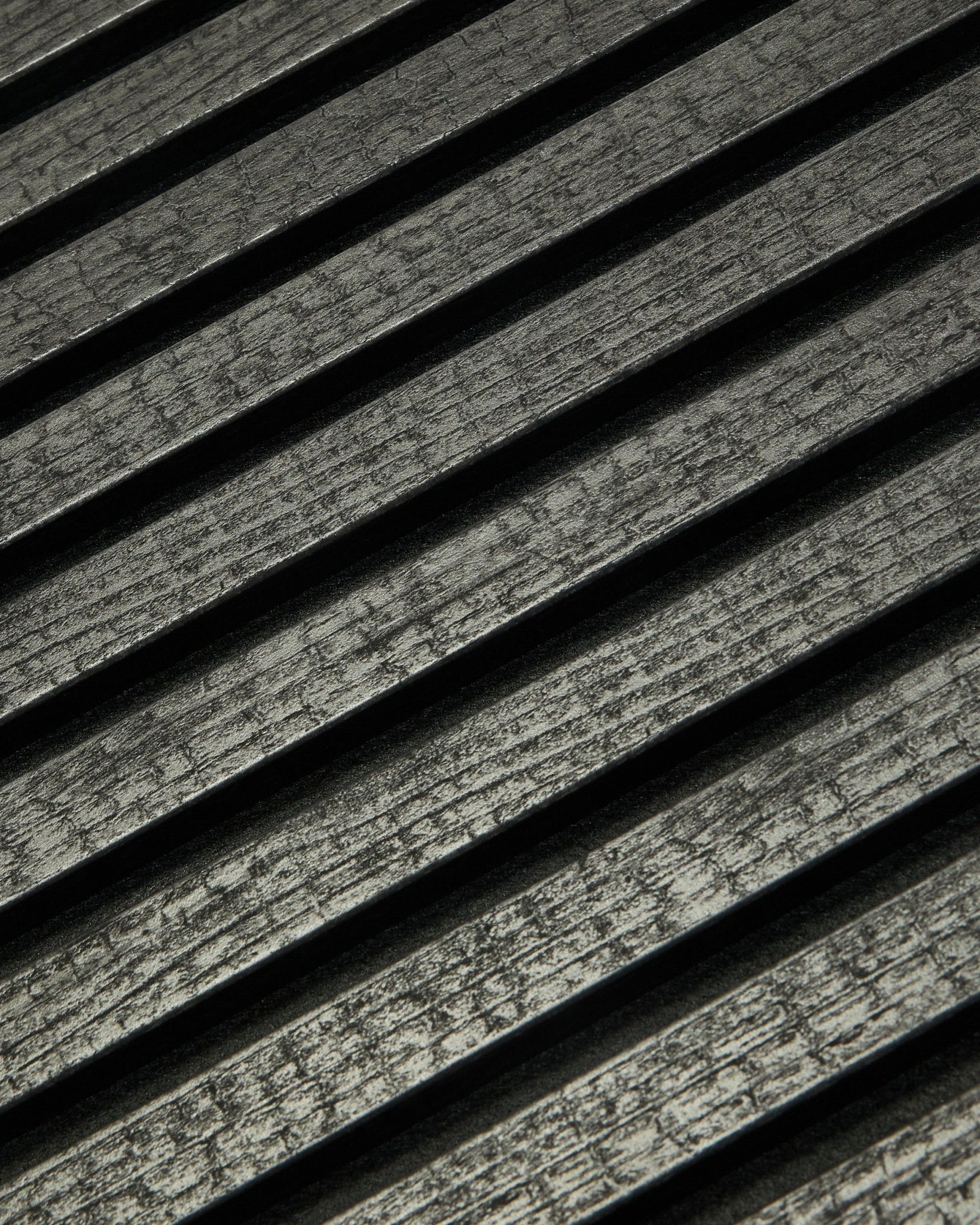 Zbliżenie na WoodUpp Rebel Akupanel w kolorze Charcoal (240x60 cm), pokazujące black, rowkowane lamele akustyczne ułożone po skosie dla lepszego pochłaniania dźwięku.