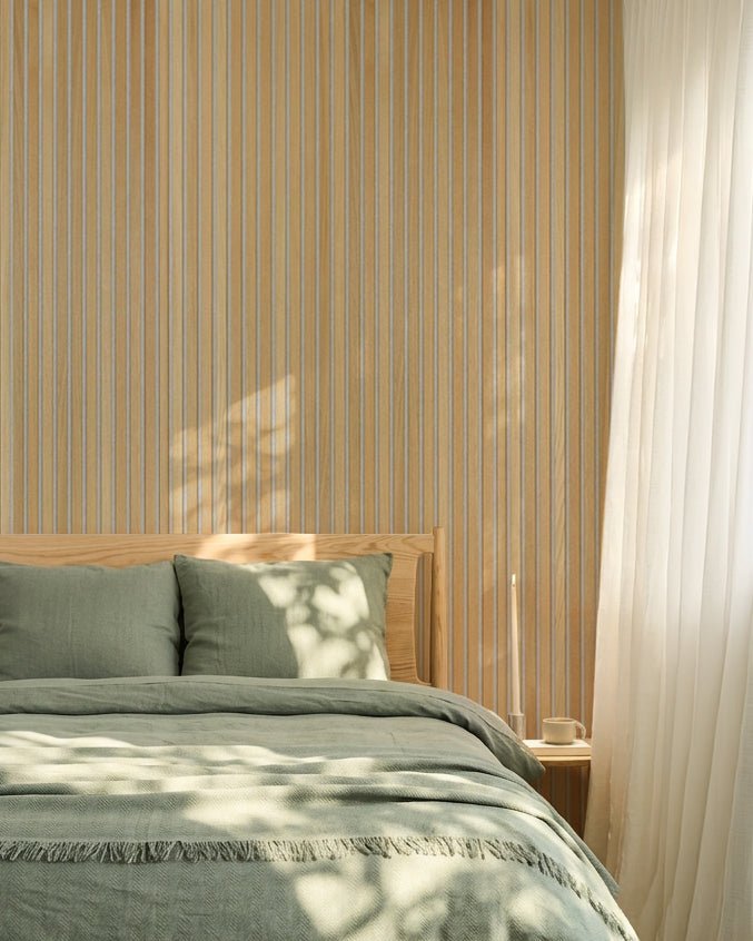 Minimalistyczna sypialnia w stylu nordyckim z pościelą w odcieniu szałwiowej zieleni i akustycznym panelem lamelowym WoodUpp Classic Oak Akupanel; światło słoneczne tworzy na łóżku miękkie cienie.