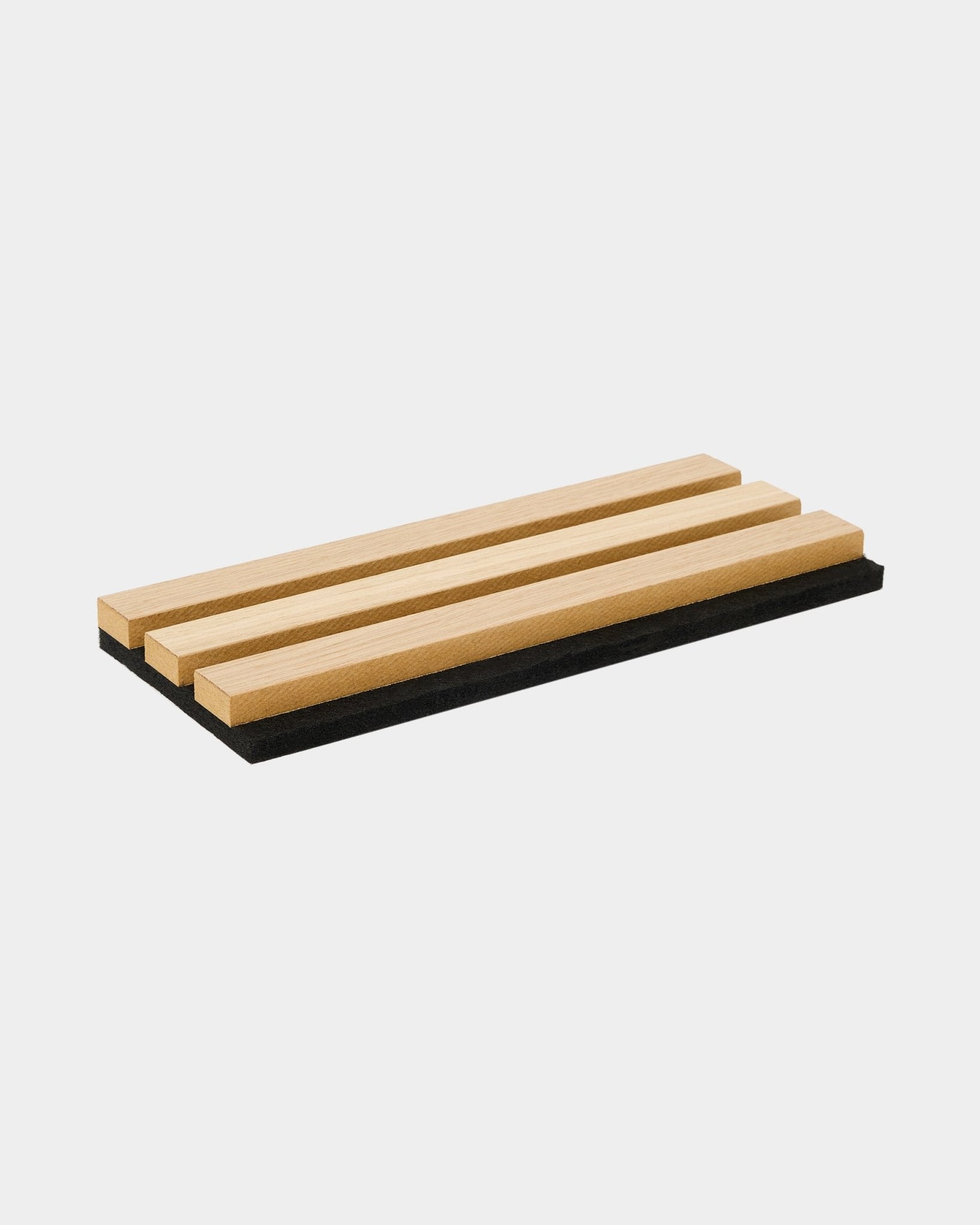 Tacka z próbką WoodUpp Akupanel w kolorze Classic Oak ma trzy akustyczne lamele drewniane na filcowej podstawie black, pokazując nordycki design i kontrast materiałów.