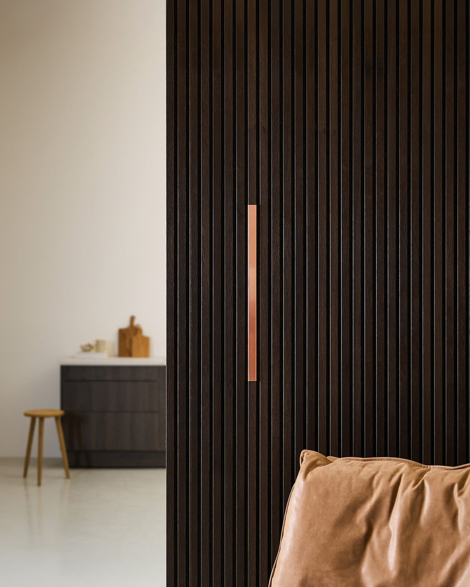 Minimalistyczna kuchnia z panelem akustycznym WoodUpp Liva | Cover / Copper na ścianie o szerokości 60 cm, krzesłem z jasnobrązowej skóry, stołkiem i blatem.