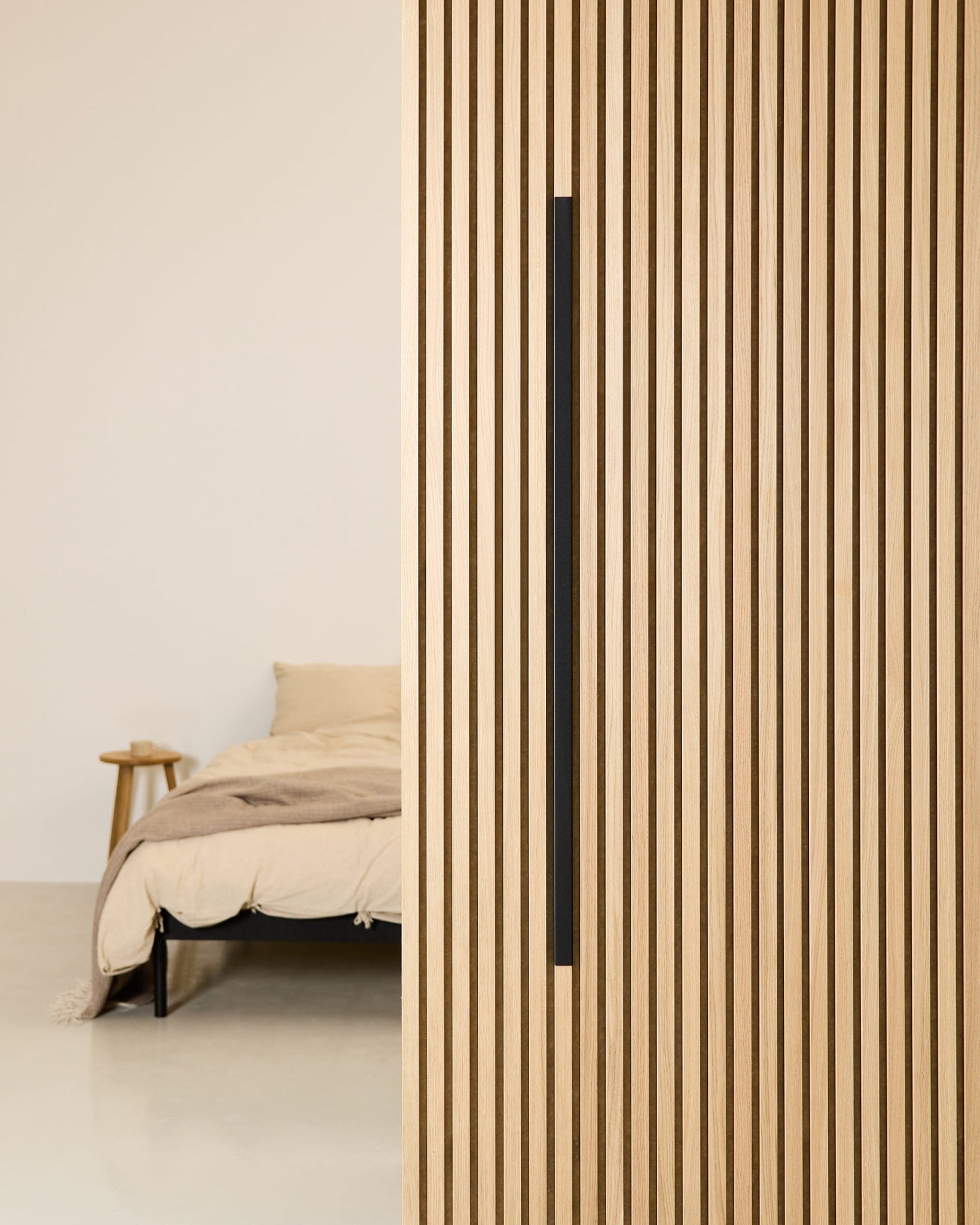 Minimalistyczna sypialnia z beżowym łóżkiem, drewnianym stolikiem nocnym oraz zamontowanym na ścianie panelem akustycznym WoodUpp Akupanel Black Aluminum o szerokości 120 cm.