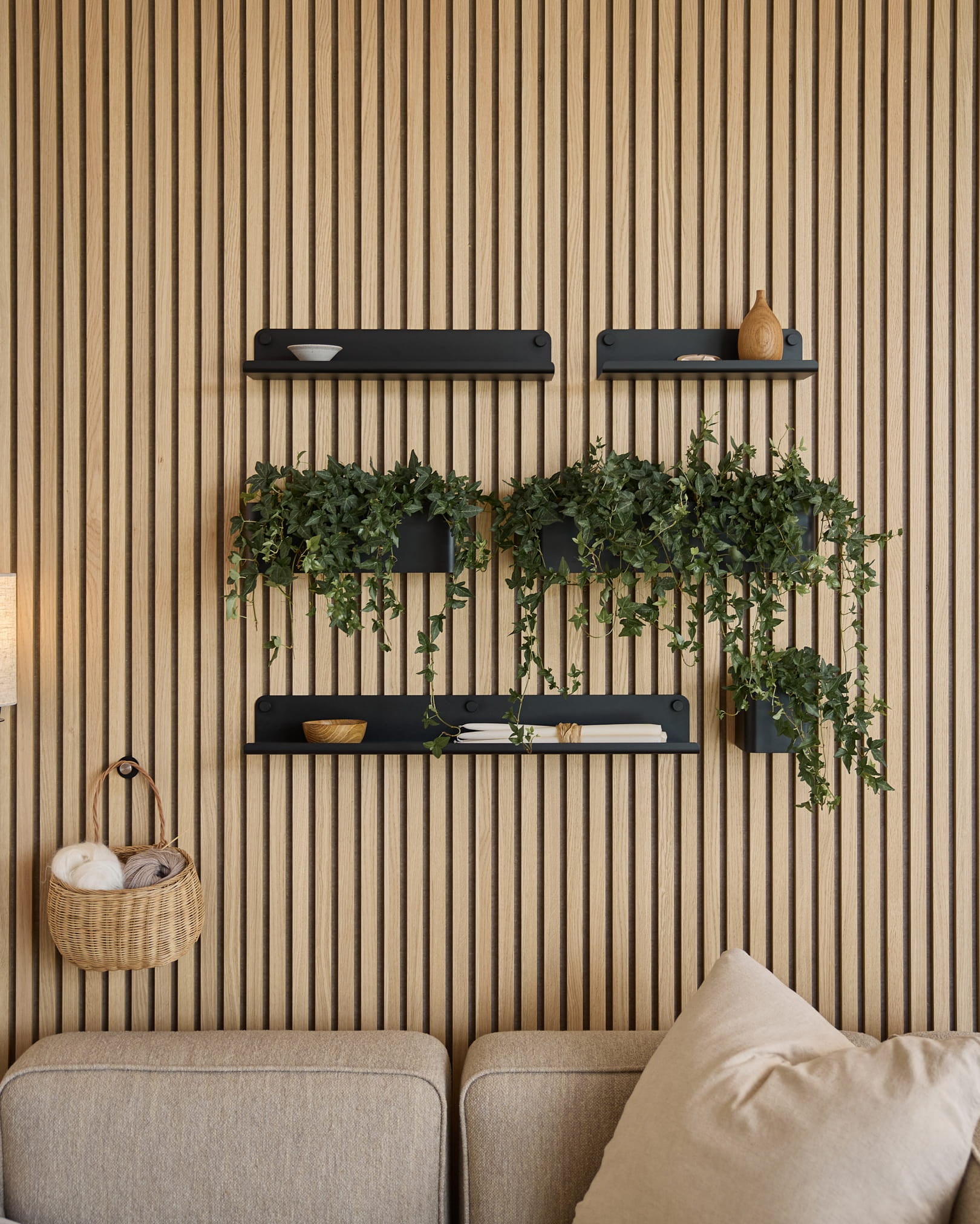 Nowoczesny salon z nordyckim akustycznym panelem lamelowym, półkami black, zwisającymi roślinami w donicy Plant Box WoodUpp Norr (35,9 cm, Black) oraz sofą beige.