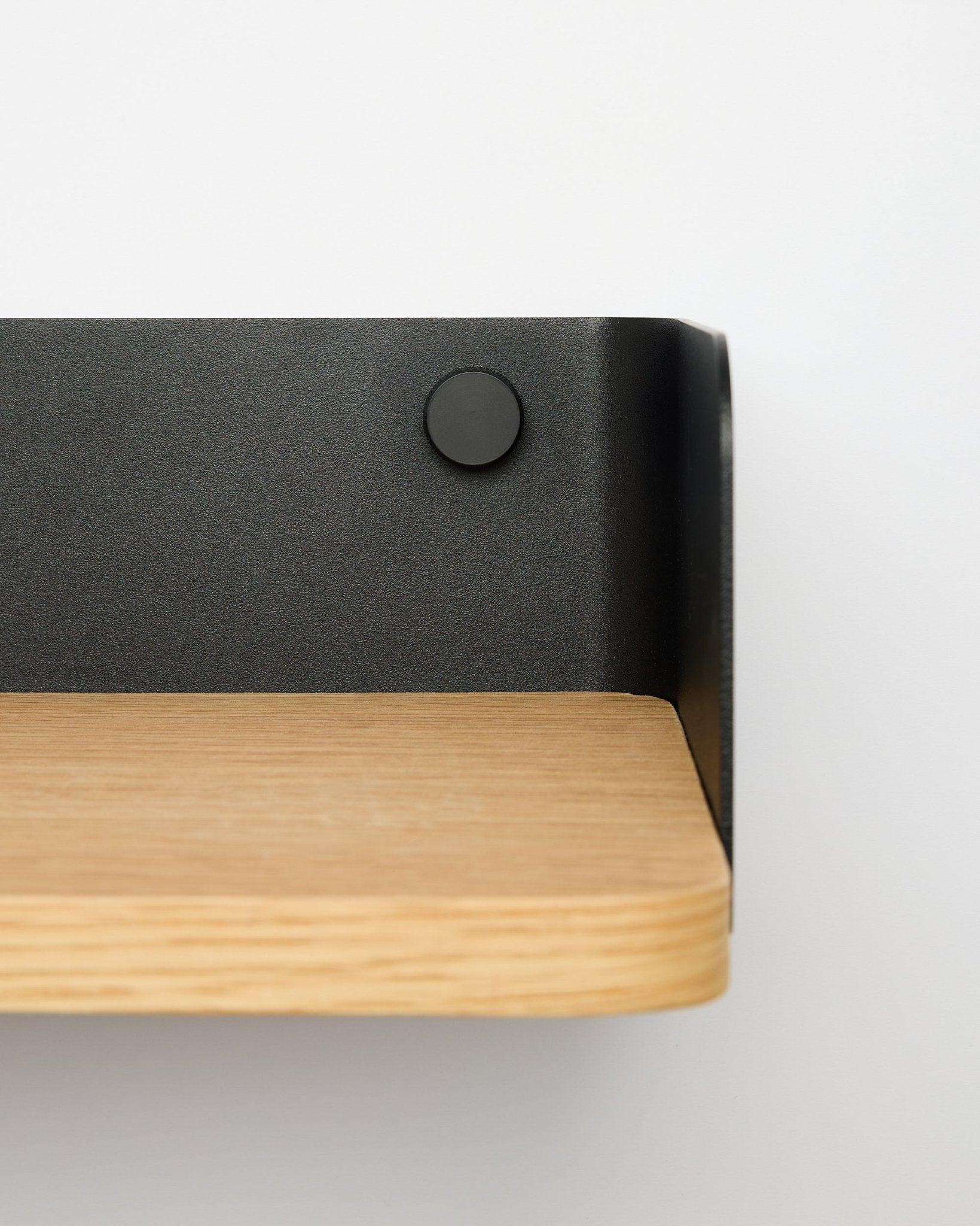 Biblioteczka Linn od WoodUpp w kolorze natural oak, o szerokości 55,9 cm, z metalowym wspornikiem black, zamontowana na białej ścianie; zbliżenie z prawej strony.