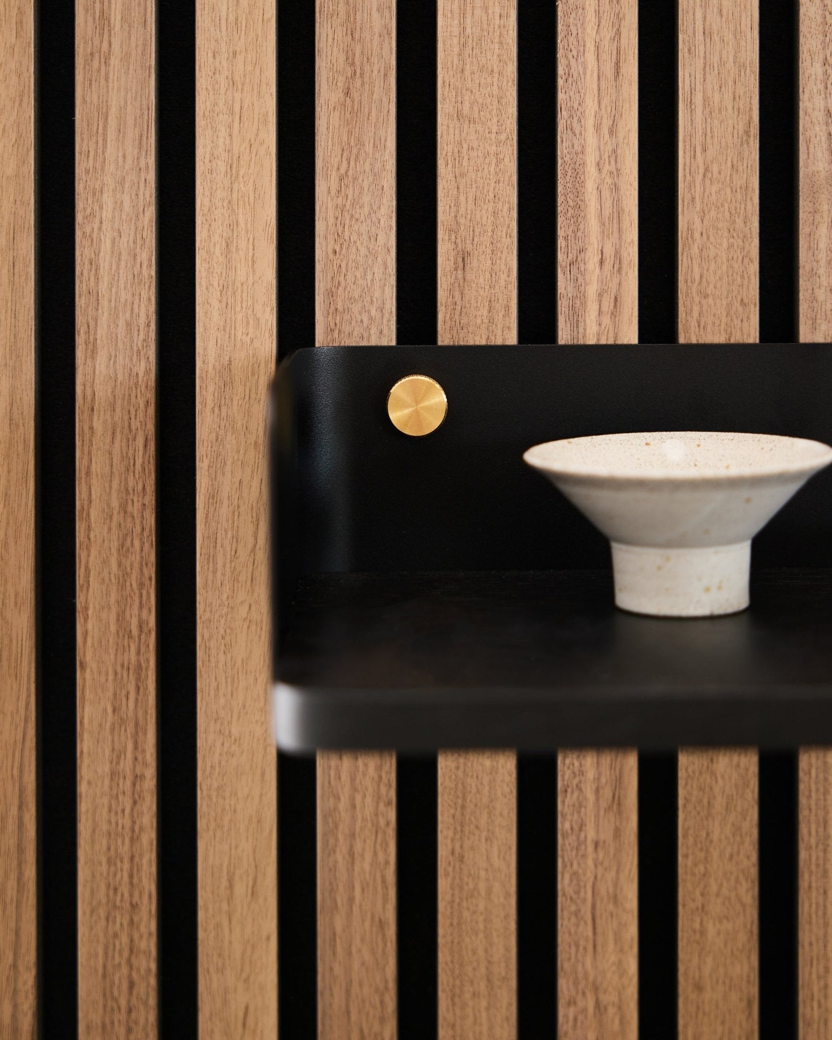 Ceramiczna miska ustawiona na biblioteczce Linn od WoodUpp, 39,9 cm w kolorze black oak, z lamelami vertical black i akcentem brass, nawiązująca do nordyckiego minimalistycznego wzornictwa.