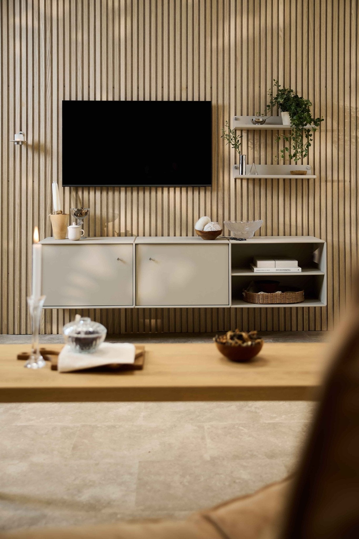Nowoczesny salon z szafką pod telewizor „Arka” marki WoodUpp, modułową kanapą, półkami w stylu skandynawskim z roślinami i dekoracjami oraz świecą na stoliku kawowym.