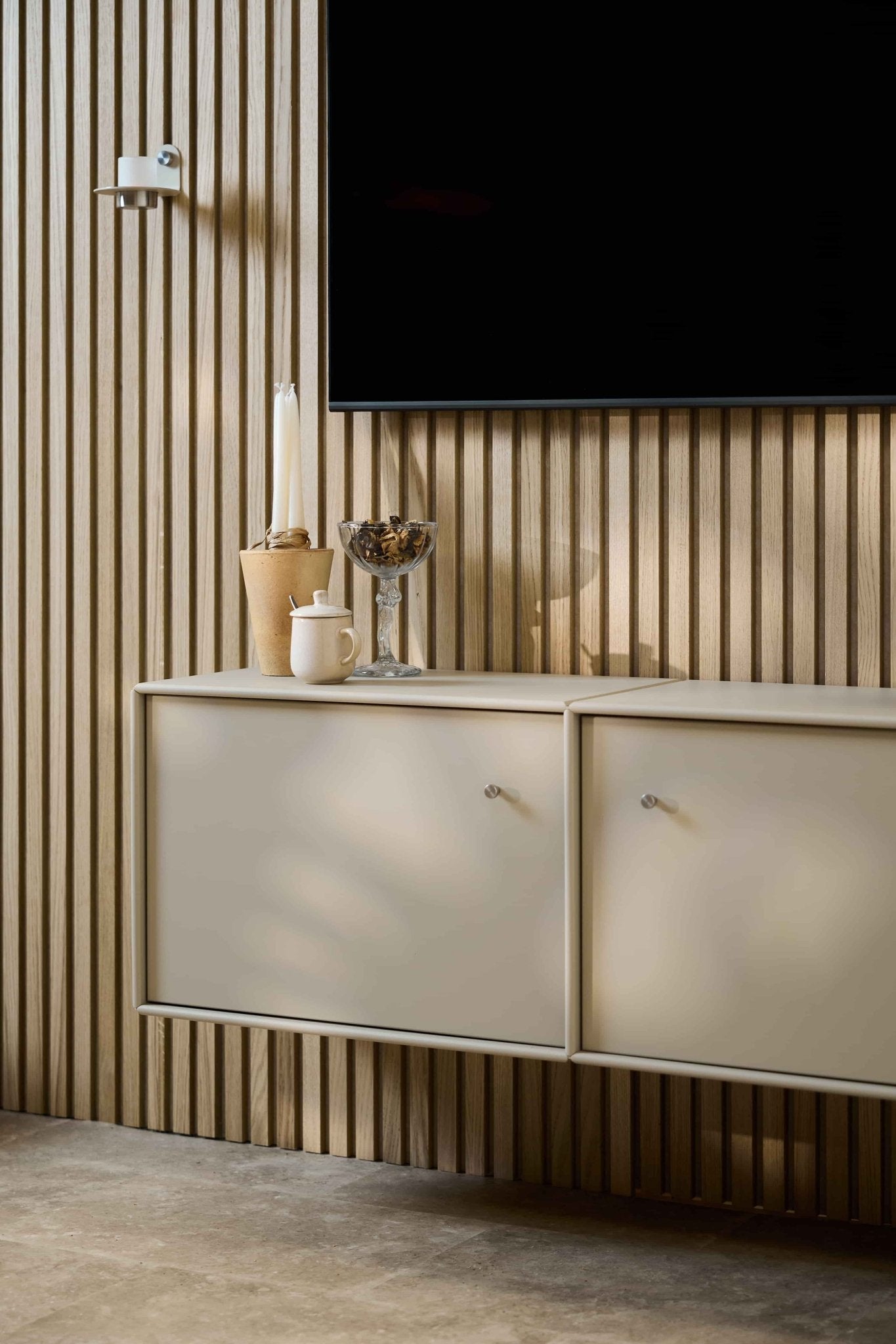 Minimalistyczny salon z konsolą pod telewizor WoodUpp Arka w kolorze beżowym, ścianą z akustycznych paneli drewnianych Akupanel, telewizorem zamontowanym na ścianie, świecami, szklaną miską, białym słoikiem oraz schludnie uporządkowanymi kablami.