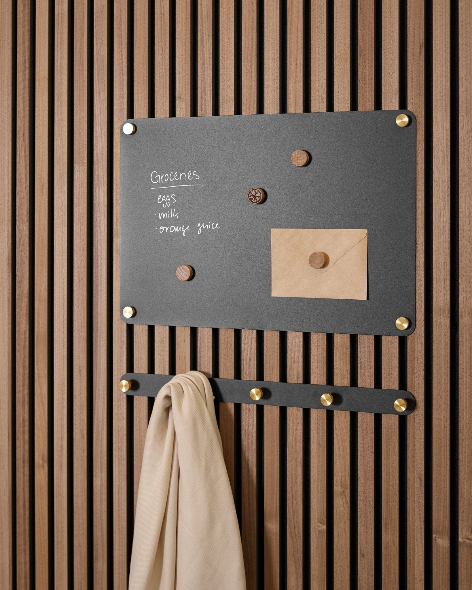 small black Norr tablica magnetyczna WoodUpp mieści listę zakupów, kopertę, magnesy i beige tkaninę na haczykach, zamontowana na Akupanel Panel akustyczny.