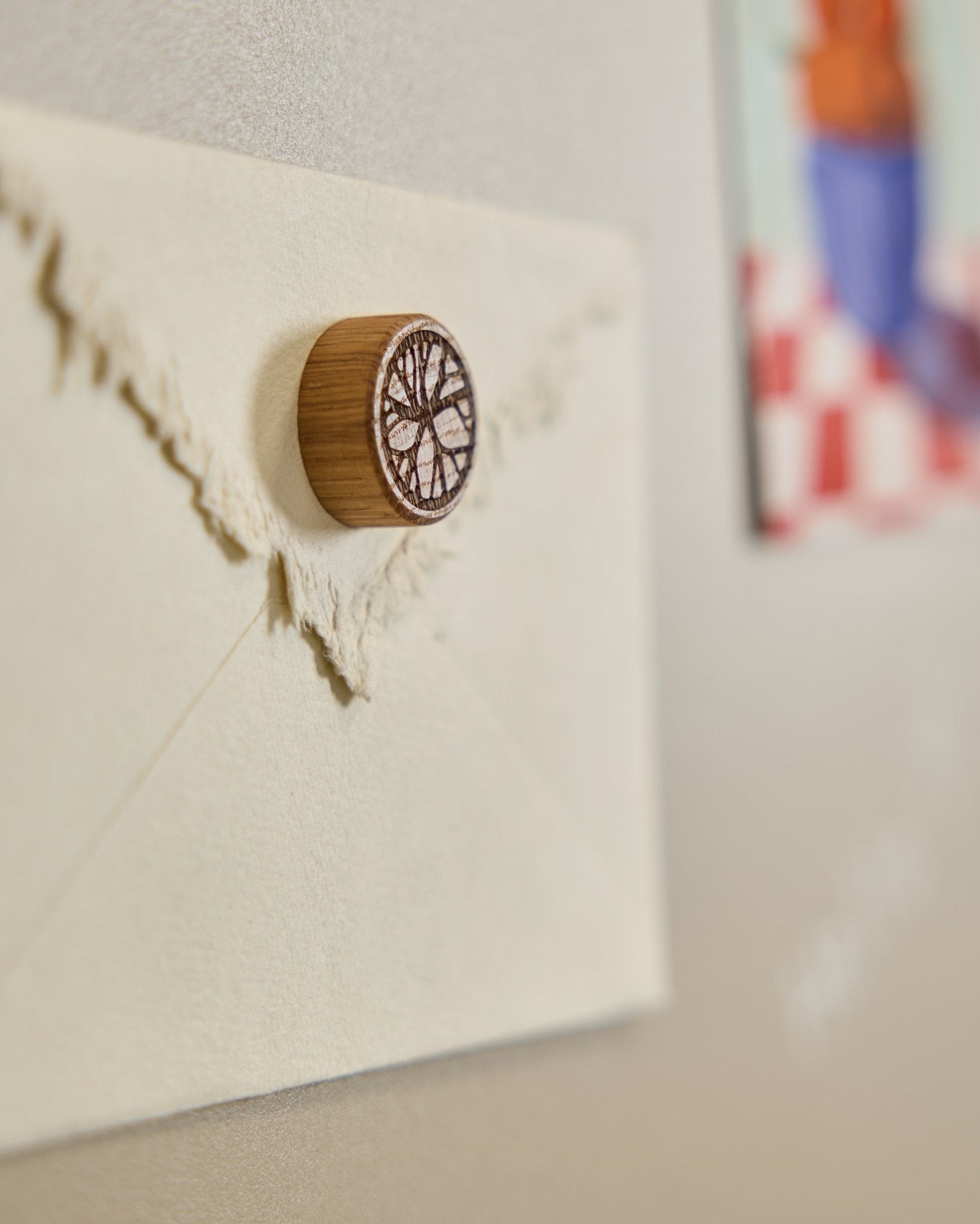 Kremowa koperta jest przypięta do Panel akustyczny za pomocą magnesu WoodUpp Norr Natural Oak, ozdobionego minimalistycznym motywem drzewa.
