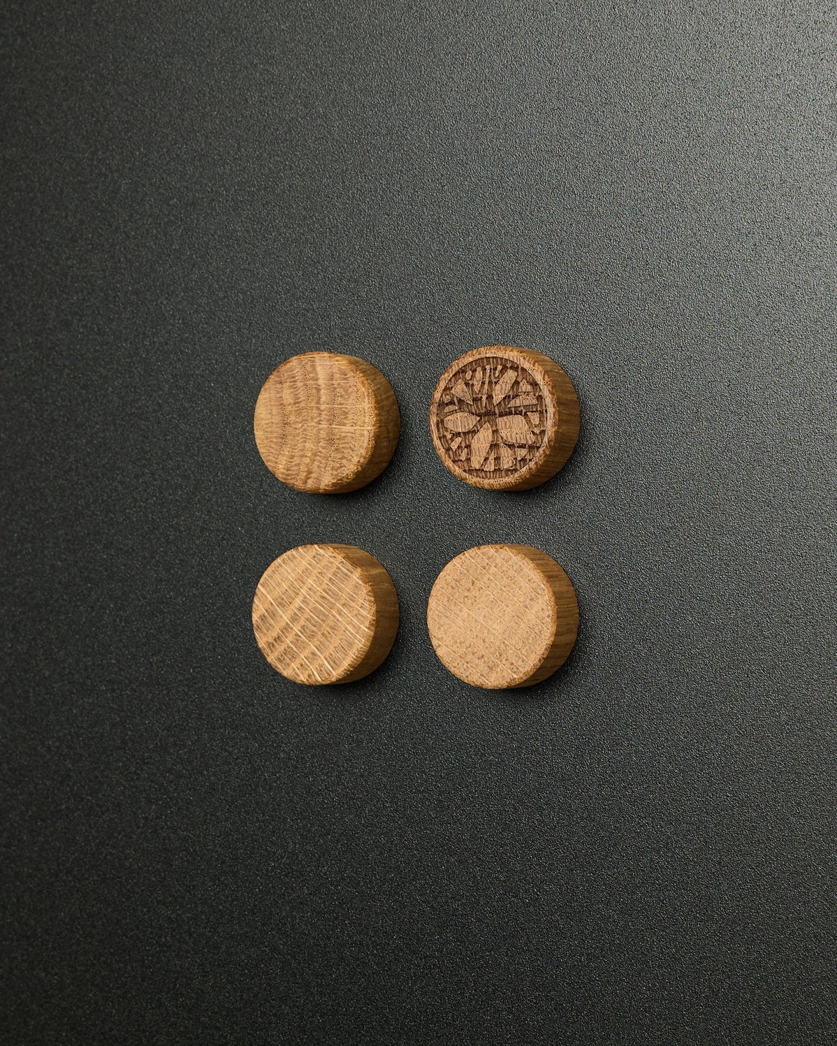 Zestaw czterech litych magnesów natural oak od WoodUpp, z których jeden ma rzeźbiony wzór plastra cytrusa, przeznaczony do tablicy magnetycznej Norr Panel akustyczny.