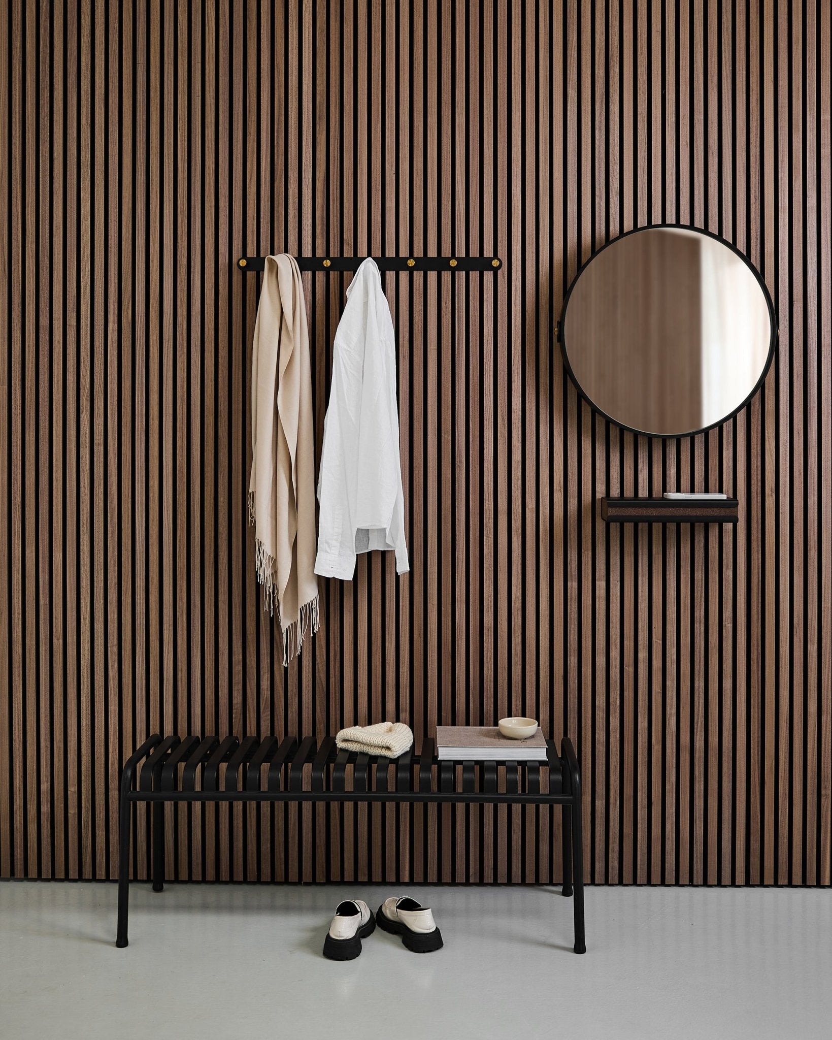Minimalistyczny przedpokój z WoodUpp Linn | Mirror w kolorze Black Oak, nordyckim akustycznym panelem ściennym z lamelami, ławką, półką, wiszącym płaszczem i szalikiem oraz butami na podłodze.