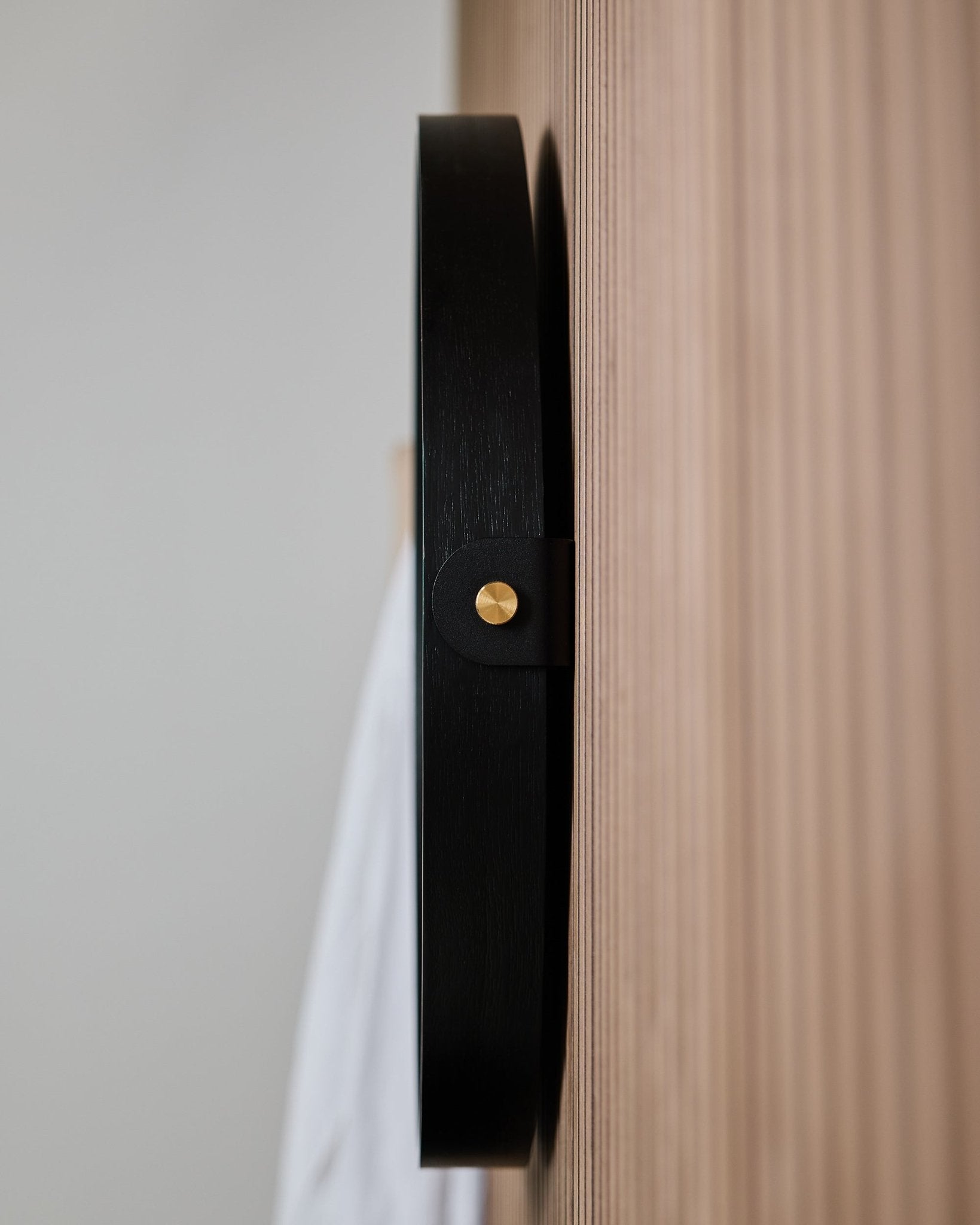 Zbliżenie z boku na ścienny hak WoodUpp Linn | Mirror / Black Oak, zamontowany na rowkowanym dębowym Panel akustyczny, zaprojektowany do zawieszenia okrągłego lustra.