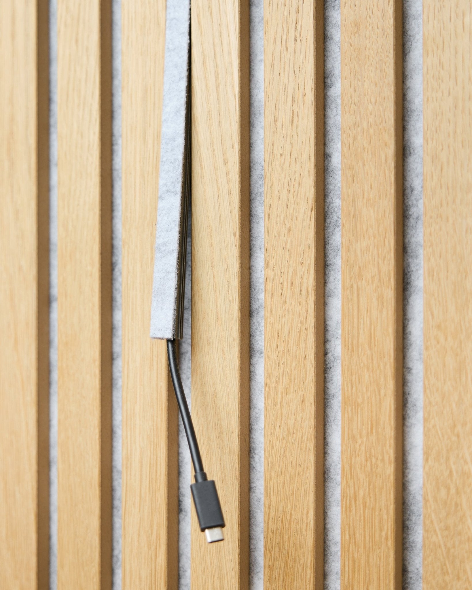 black kabel USB-C biegnie przez grey osłonę kabli Pop-on WoodUpp Dupps między vertical drewnianymi listwami akustycznymi z grey filcowym podkładem.