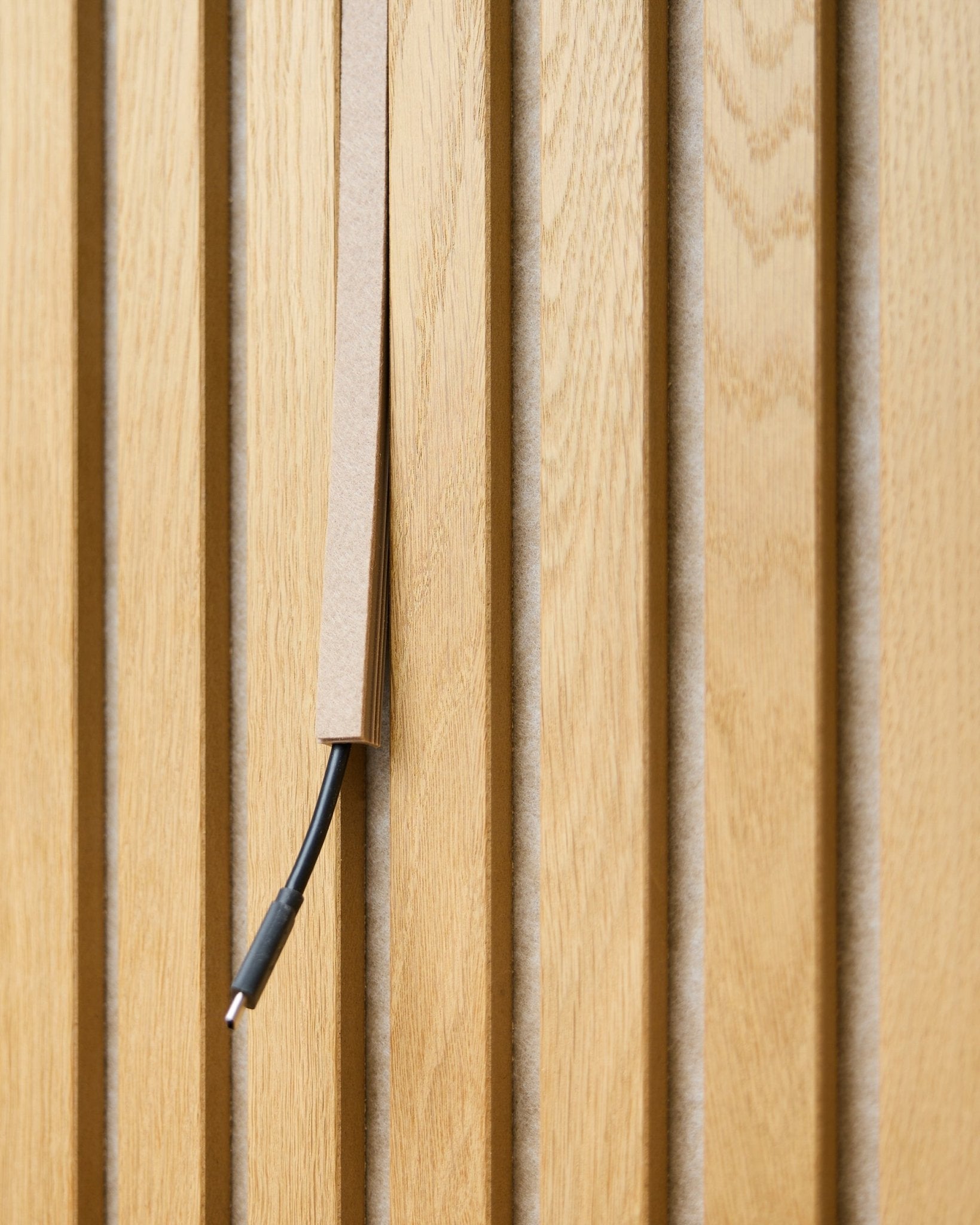 black kabel z systemem organizacji przewodów jest częściowo ukryty w osłonie na kabel Pop-on WoodUpp Dupps Beige, zamontowanej na vertical Akupanel akustycznych lamelach drewnianych.