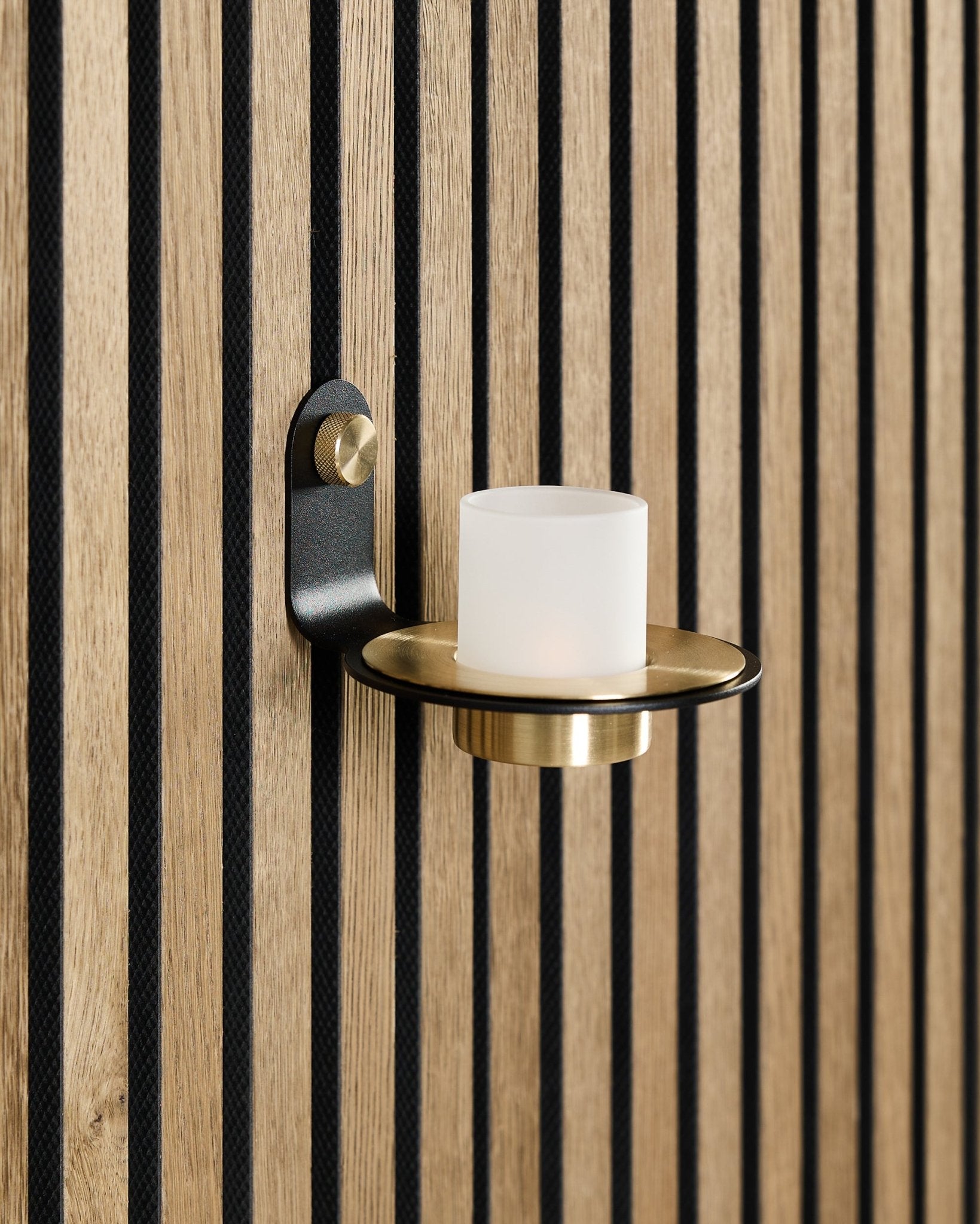 Świecznik Norr w kolorach black i brass od WoodUpp jest zamontowany na nordyckim akustycznym panelu drewnianym Akupanel z listwami black w kolorze vertical.