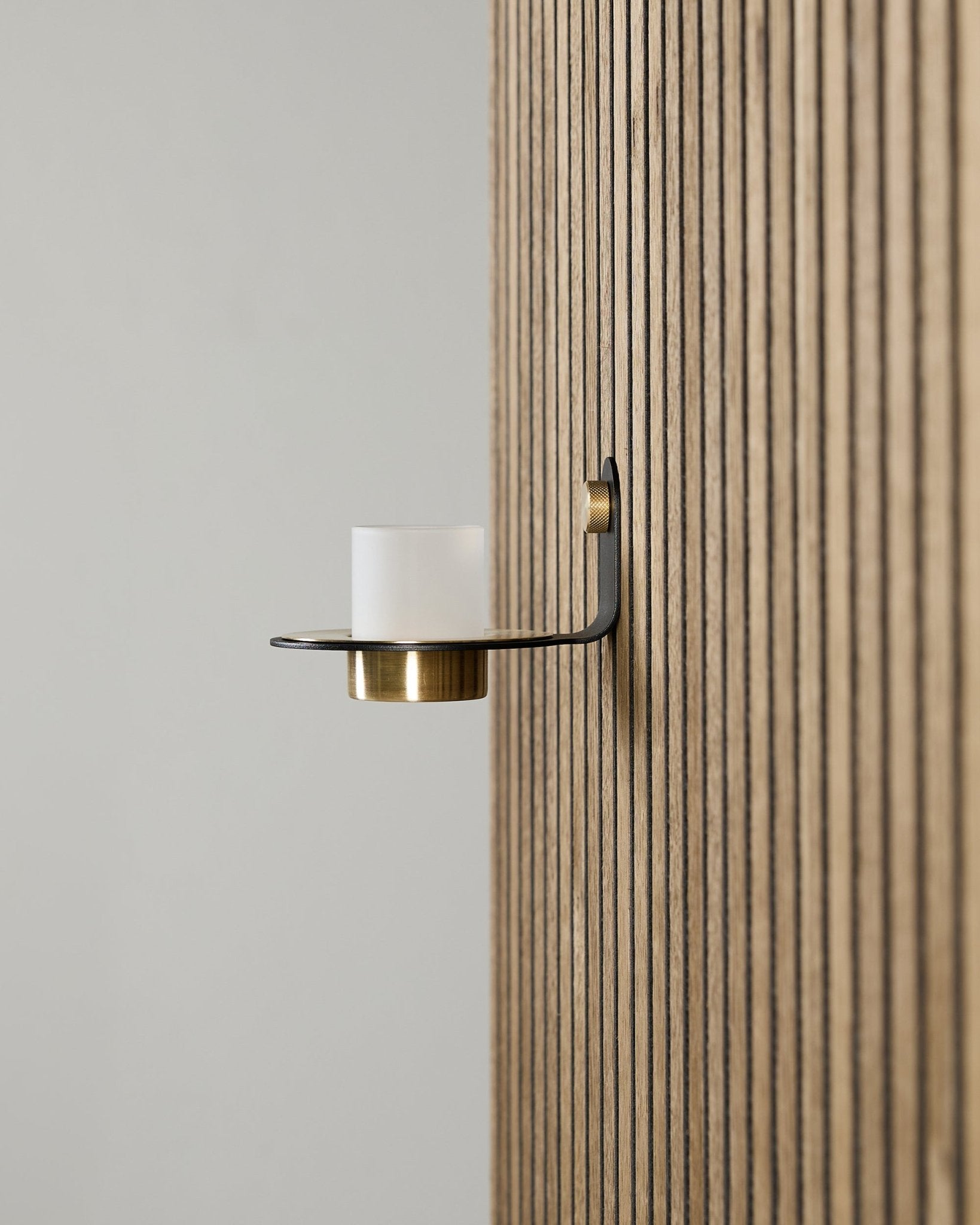 Świecznik Norr w kolorach black i brass od WoodUpp, zamontowany na vertical Akupanel Panel akustyczny, z mrożonym szkłem i detalami w kolorze brass.