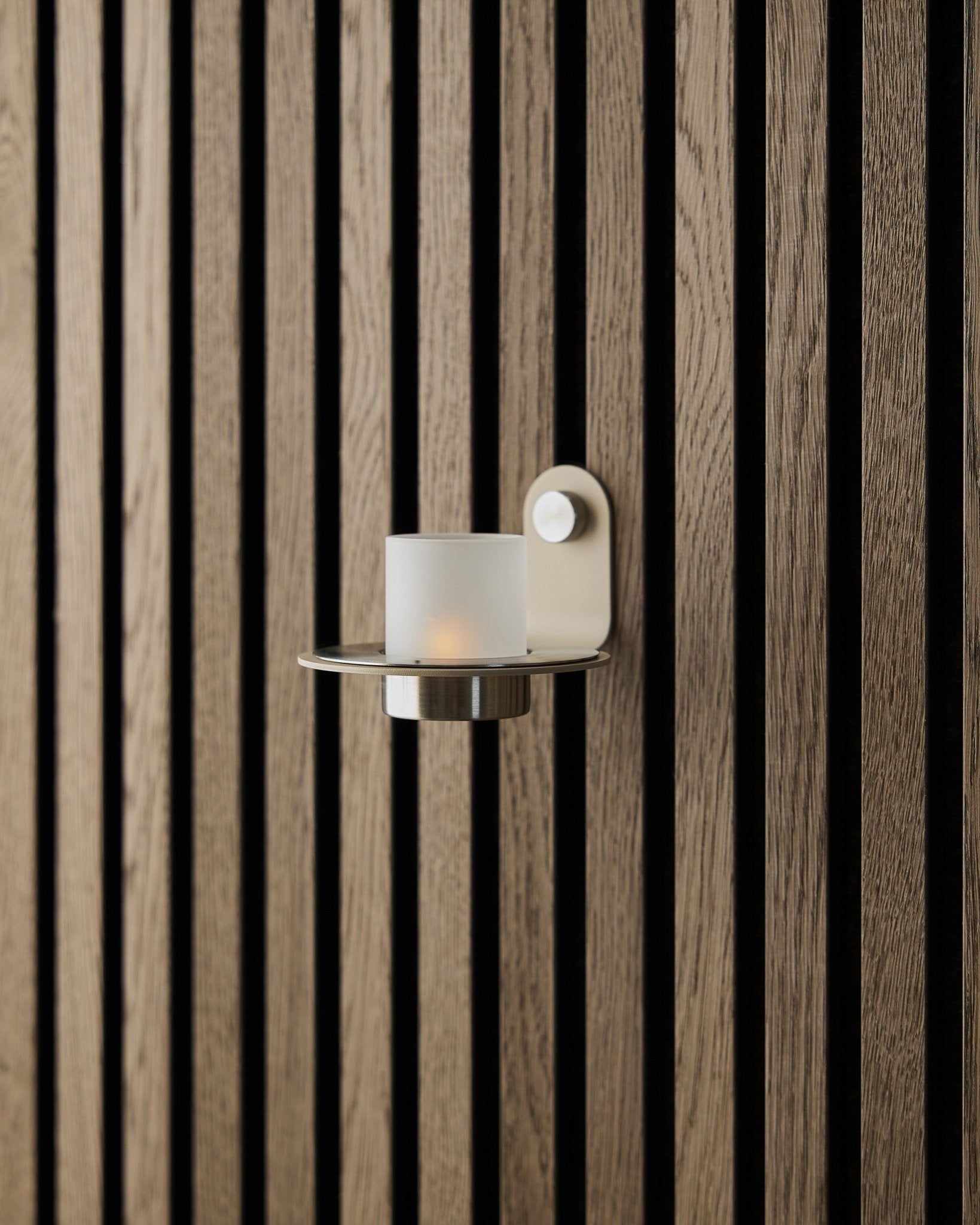 Świecznik Norr w wykończeniu ze stali nierdzewnej beige steel od WoodUpp, wyeksponowany na ścianie z beige Akupanel Panel akustyczny.