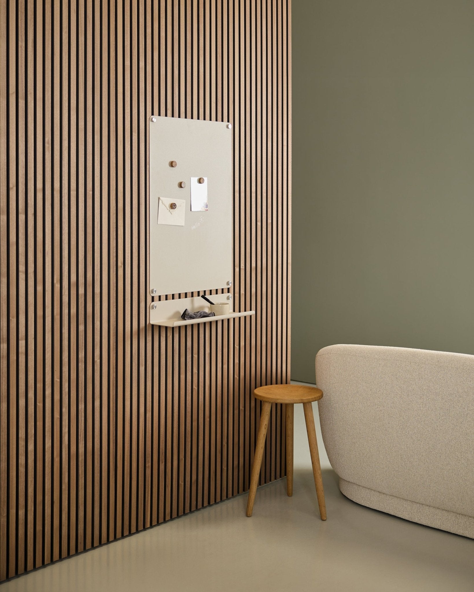 Minimalistyczne wnętrze z sofą beige i drewnianym stołkiem, z zamontowaną tablicą magnetyczną WoodUpp large beige Norr na nordyckim panelu akustycznym z drewna Akupanel przy zielonej ścianie.
