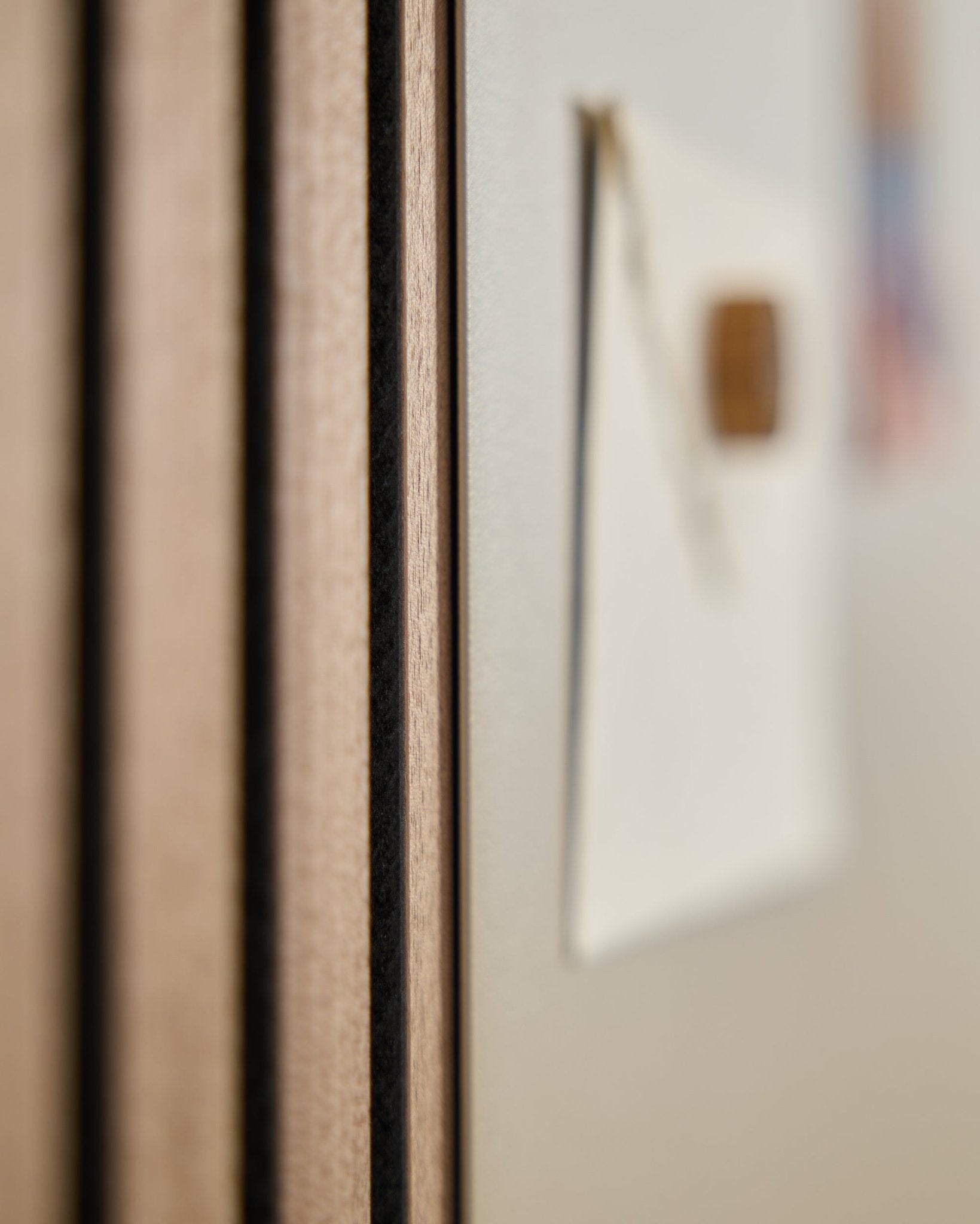 Zbliżenie na panel akustyczny z drewna WoodUpp Akupanel z listwami vertical, obok rozmytej w tle tablicy magnetycznej large beige Norr.