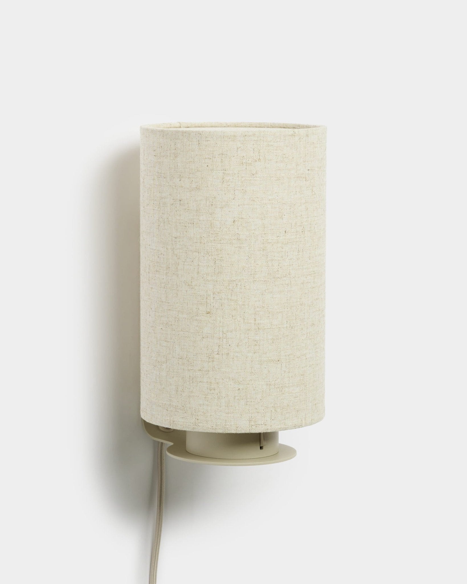 Feya | Wall Lamp od WoodUpp z cylindrycznym abażurem z lnu i bawełny oraz widocznym białym przewodem, wykończenie beige, zaprojektowana jako dopełnienie akustycznych paneli drewnianych.
