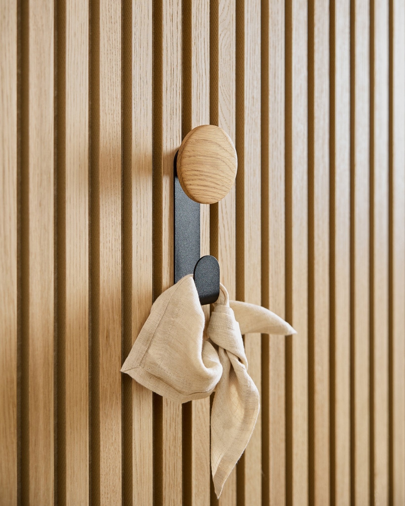 Na wieszaku Linn Vertical Hanger w kolorze Natural Oak od WoodUpp wisi beige tkanina. Wieszak zamontowano na akustycznym panelu lamelowym vertical Akupanel.