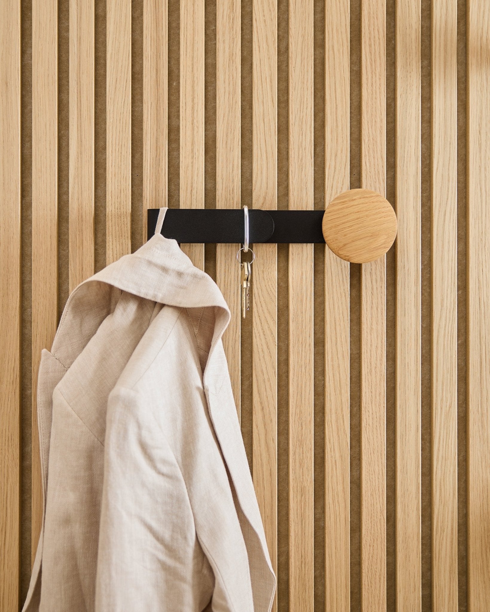 Marynarka w kolorze beige i komplet kluczy wiszą na wieszaku WoodUpp Linn Horizontal w kolorze natural oak, zamontowanym na akustycznym panelu drewnianym natural oak Akupanel.