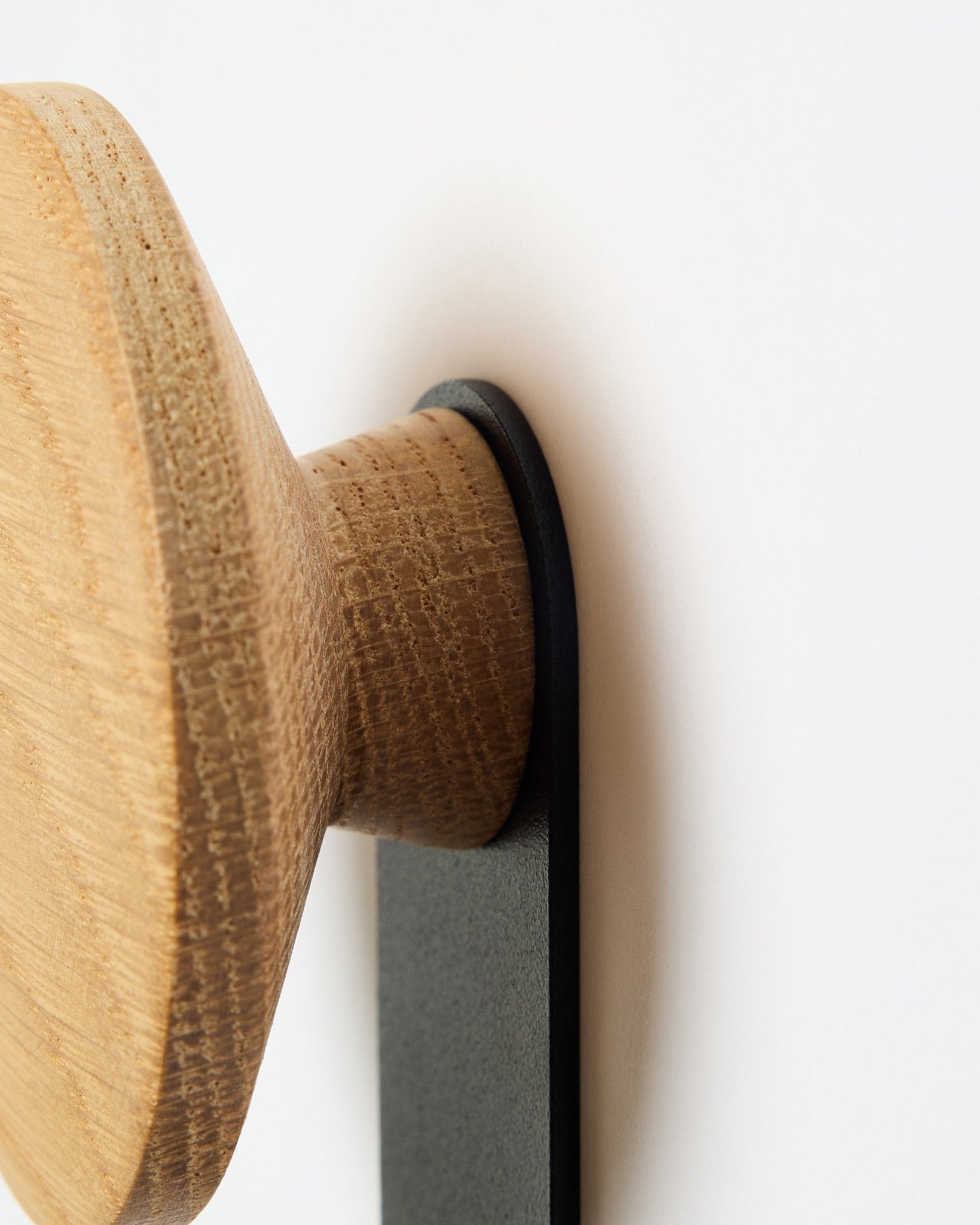 Zbliżenie na wieszak Linn Vertical Hanger w kolorze natural oak od WoodUpp. To akcesorium z okrągłym drewnianym uchwytem, zamontowane na wsporniku black, zaprojektowane do paneli akustycznych Akupanel.