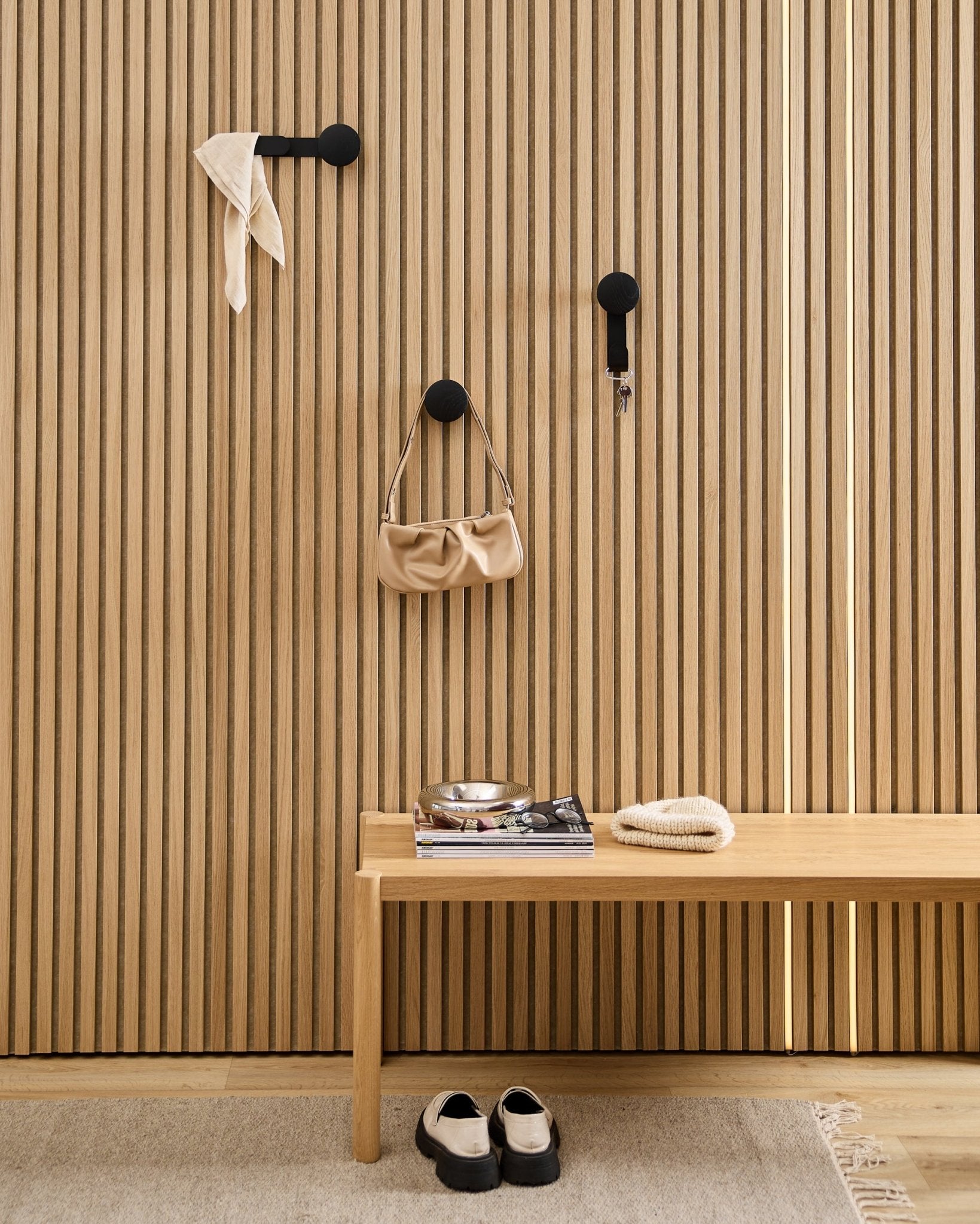 Minimalistyczny przedpokój z wieszakiem WoodUpp Linn Horizontal w kolorze Black Oak, z haczykami w odcieniu black, drewnianą ławką, butami, książkami i miseczką. Styl nordycki.