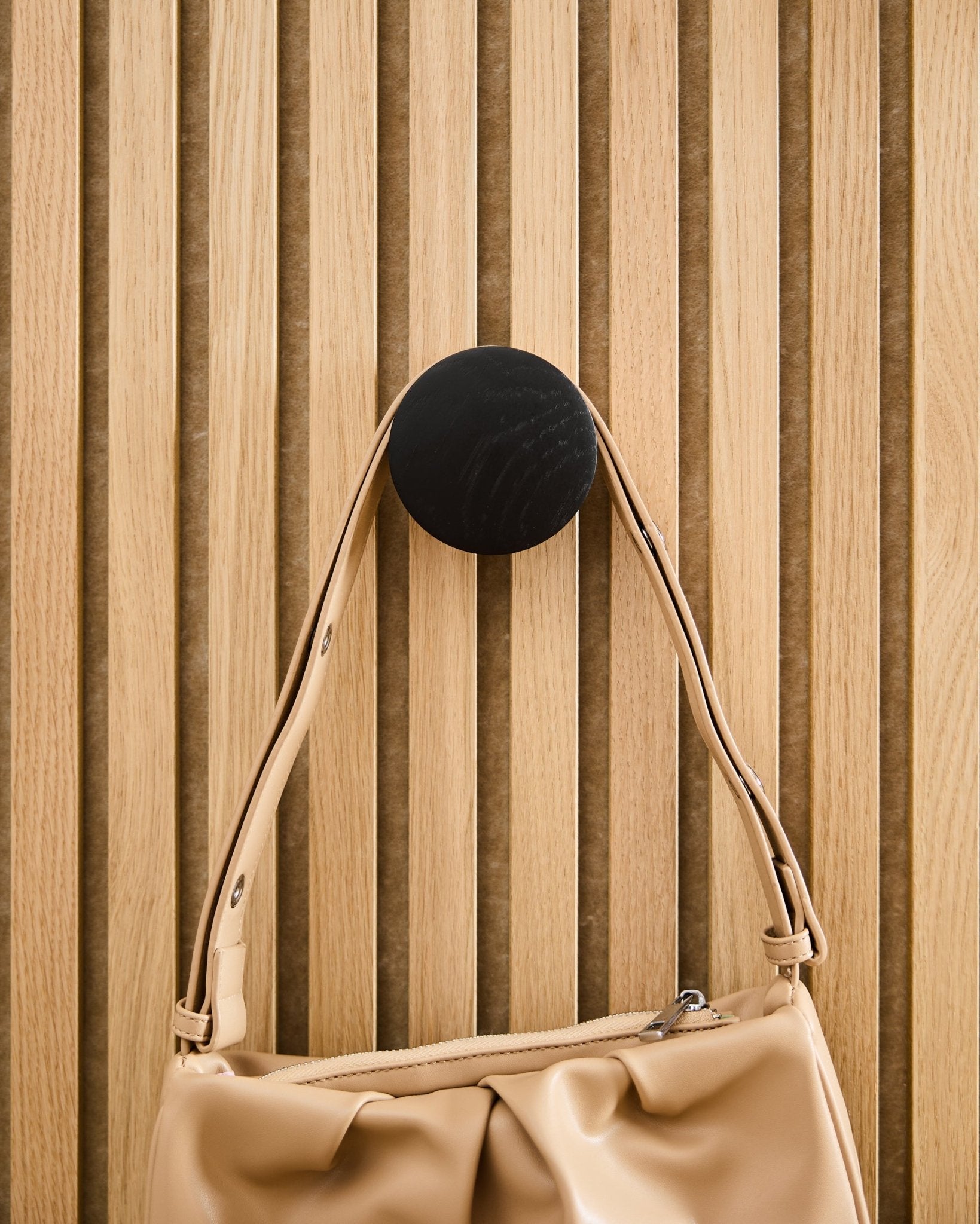 Torebka Beige zawieszona na WoodUpp Linn | Single Hanger w kolorze Black Oak, zamontowanym na jasnym drewnianym panelu akustycznym z lamelami Akupanel.