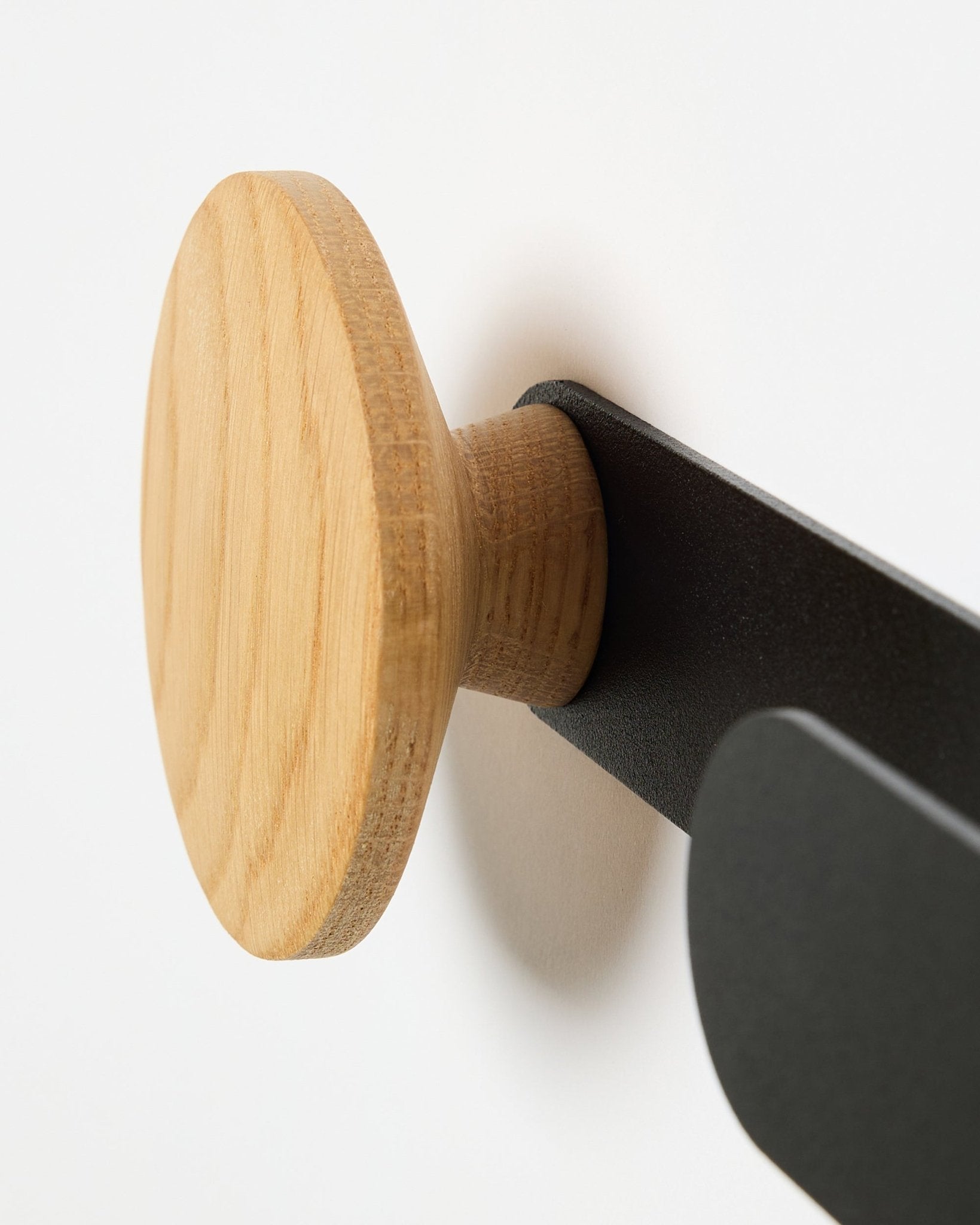 Zbliżenie na wieszak WoodUpp Linn Horizontal w kolorze natural oak, na metalowym wsporniku black, zaprojektowany do Akupanel paneli akustycznych lub jako funkcjonalny hak ścienny.