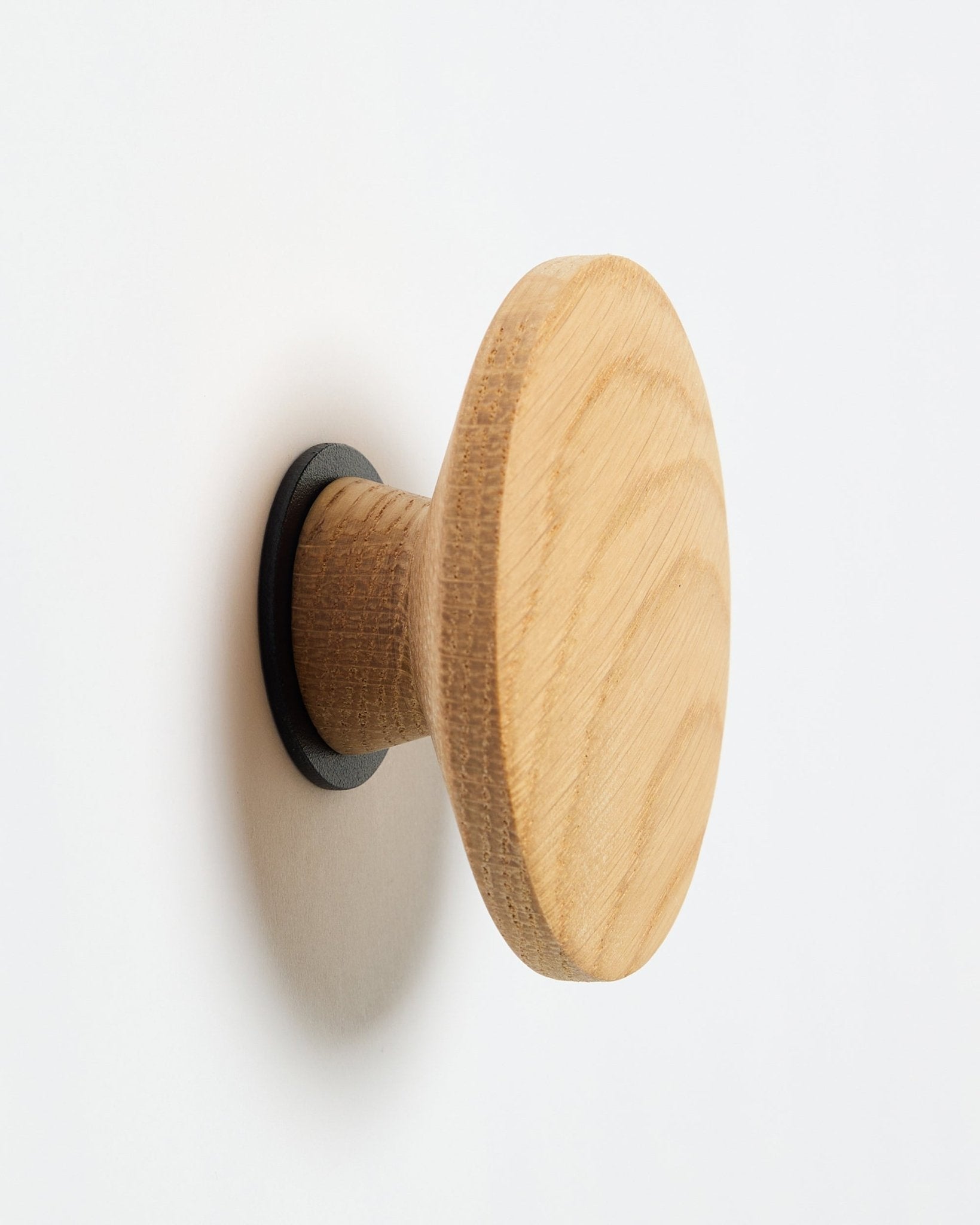 WoodUpp Linn I Single Hanger w kolorze natural oak, okrągły haczyk ścienny z black podstawą, zaprojektowany jako akcesorium do montażu na Akupanel akustycznych panelach drewnianych.