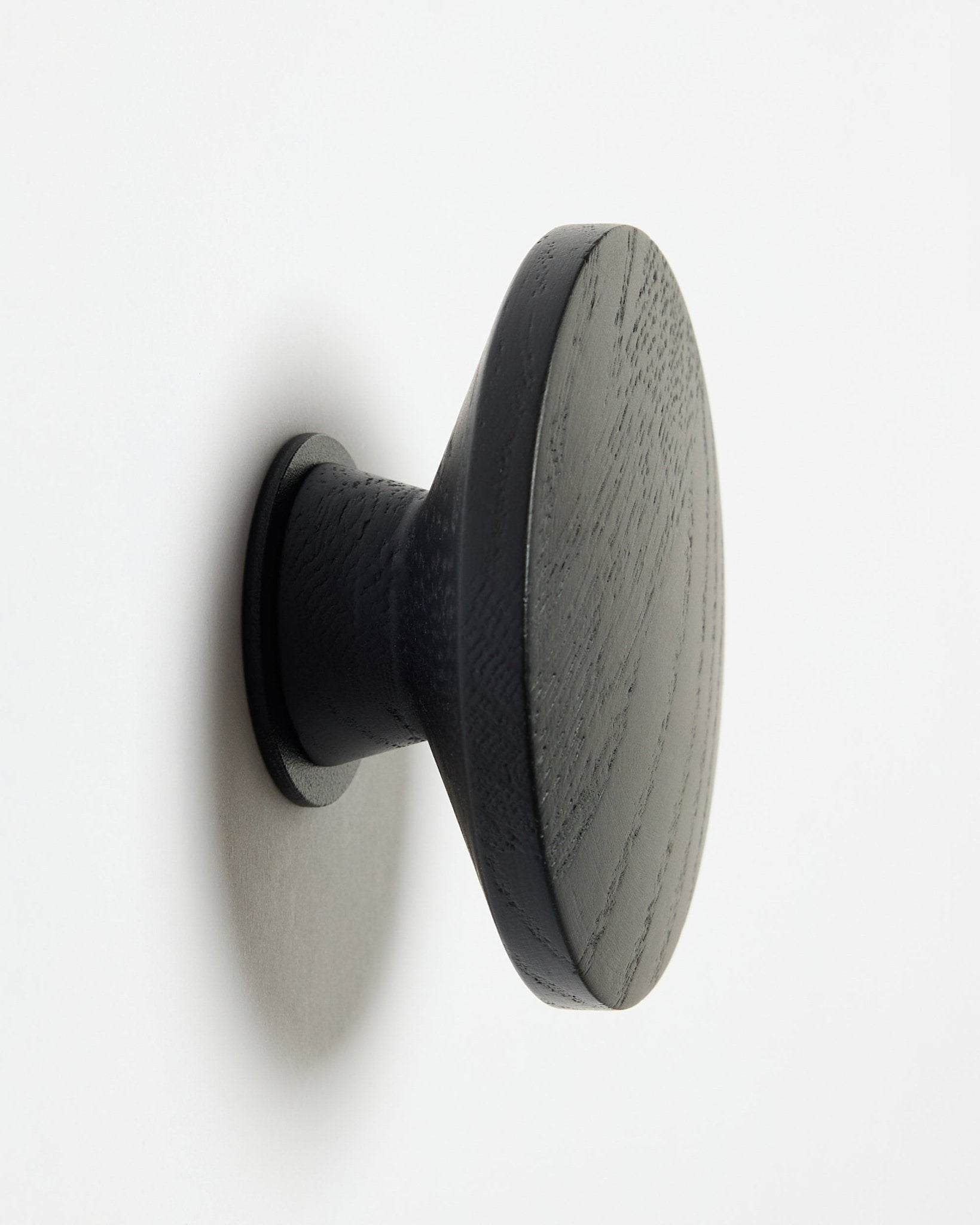 Okrągły Linn | Single Hanger WoodUpp w kolorze black oak, zaprojektowany jako dodatek do akustycznych paneli drewnianych Akupanel, zamontowany na białej powierzchni z delikatnym cieniem po lewej stronie.