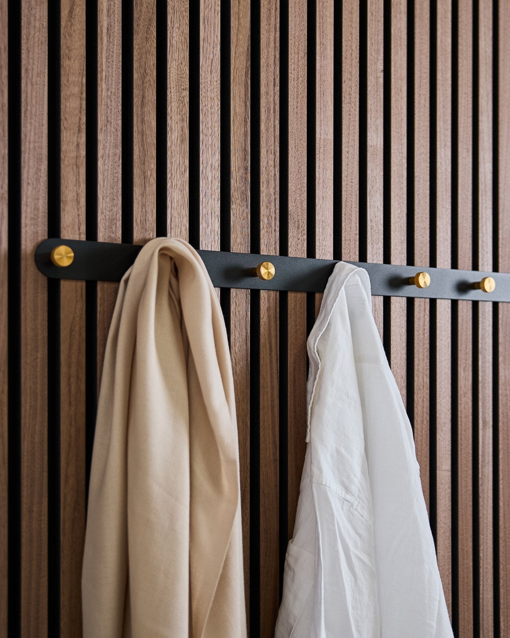 Wieszak Coat Hook Rack WoodUpp Norr w kolorze black/brass (X7) z beige szalikiem i białą koszulą zawieszony na nordyckim drewnianym akustycznym panelu lamelowym.