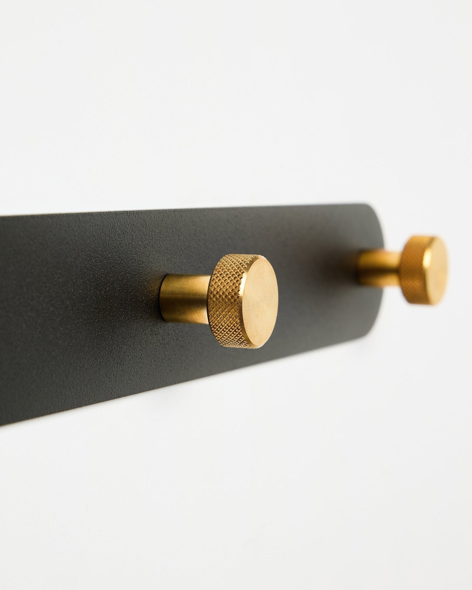 Wieszak Coat Hook Rack WoodUpp Norr, model X7, z dwoma cylindrycznymi haczykami black i brass na mocowaniu black, pokazany na białym tle.