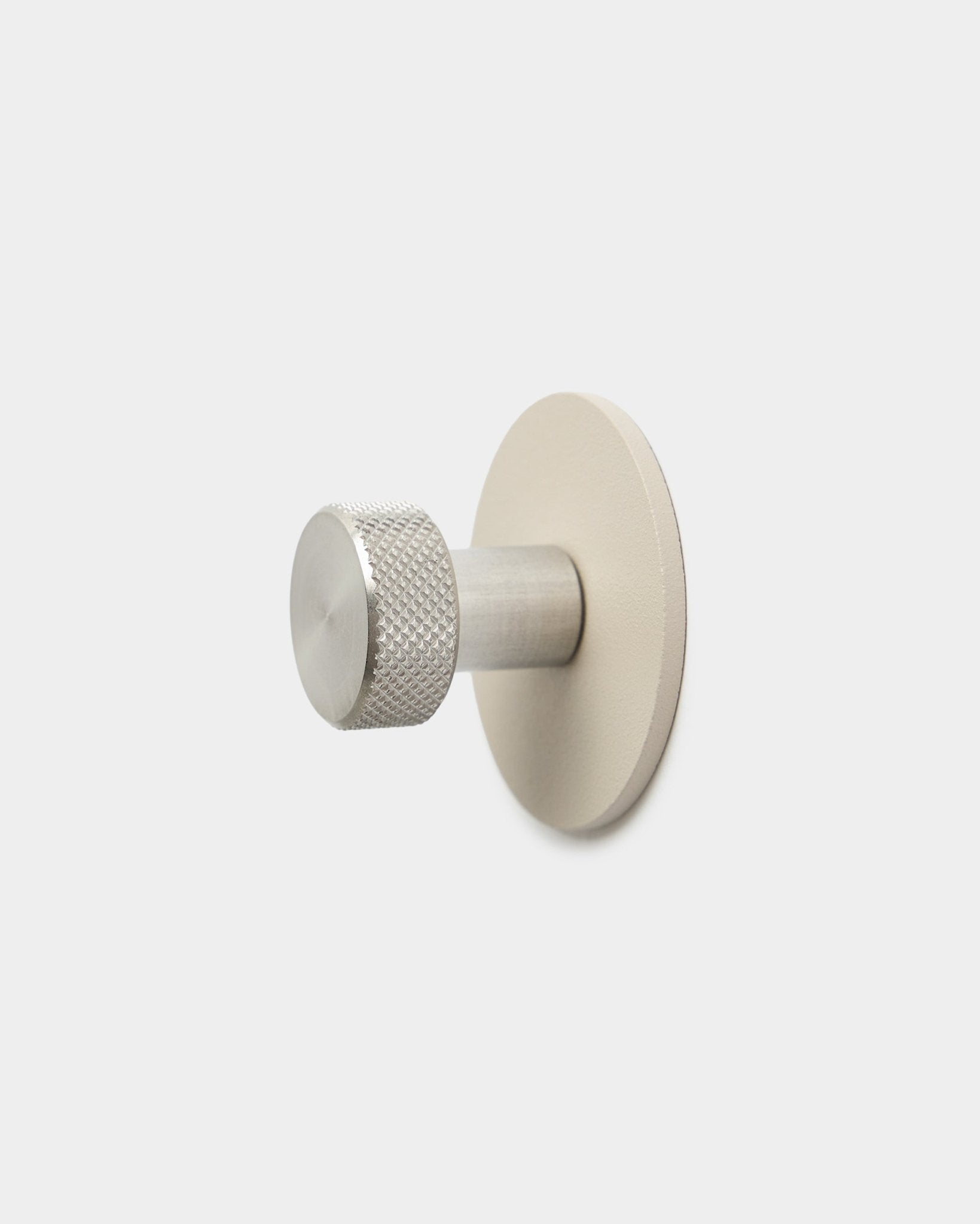 Wieszak WoodUpp Norr Coat Hook w kolorze beige i ze stali nierdzewnej steel, z fakturowanym cylindrycznym zakończeniem i okrągłą podstawą, to akcesorium do Akupanel, na jednolitym białym tle.