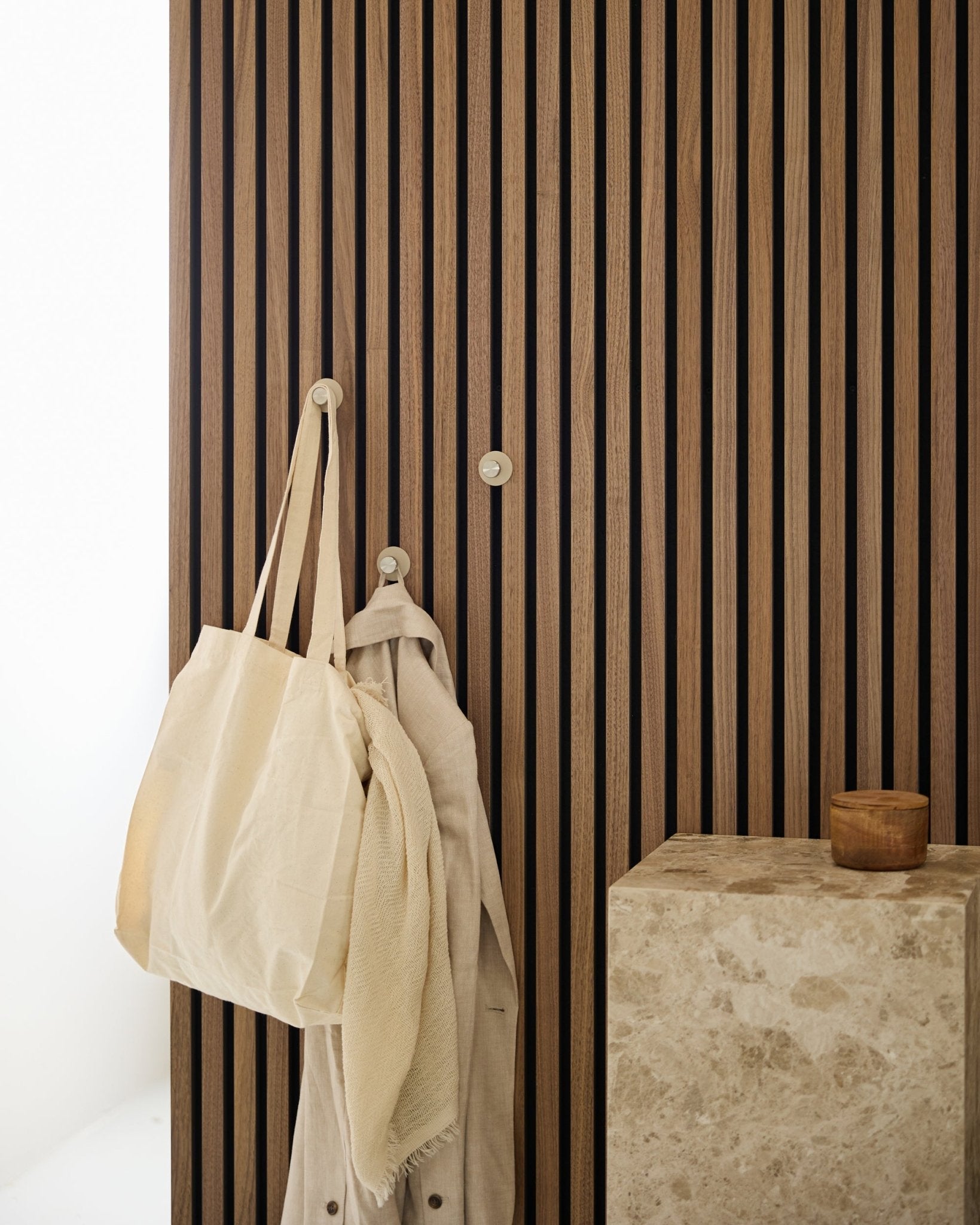 Torba typu tote w kolorze beige i jasna tkanina wiszą na wieszaku WoodUpp Norr Coat Hook (Beige/stal nierdzewna Steel), zamontowanym na vertical Akupanel Panel akustyczny obok kamiennej powierzchni.
