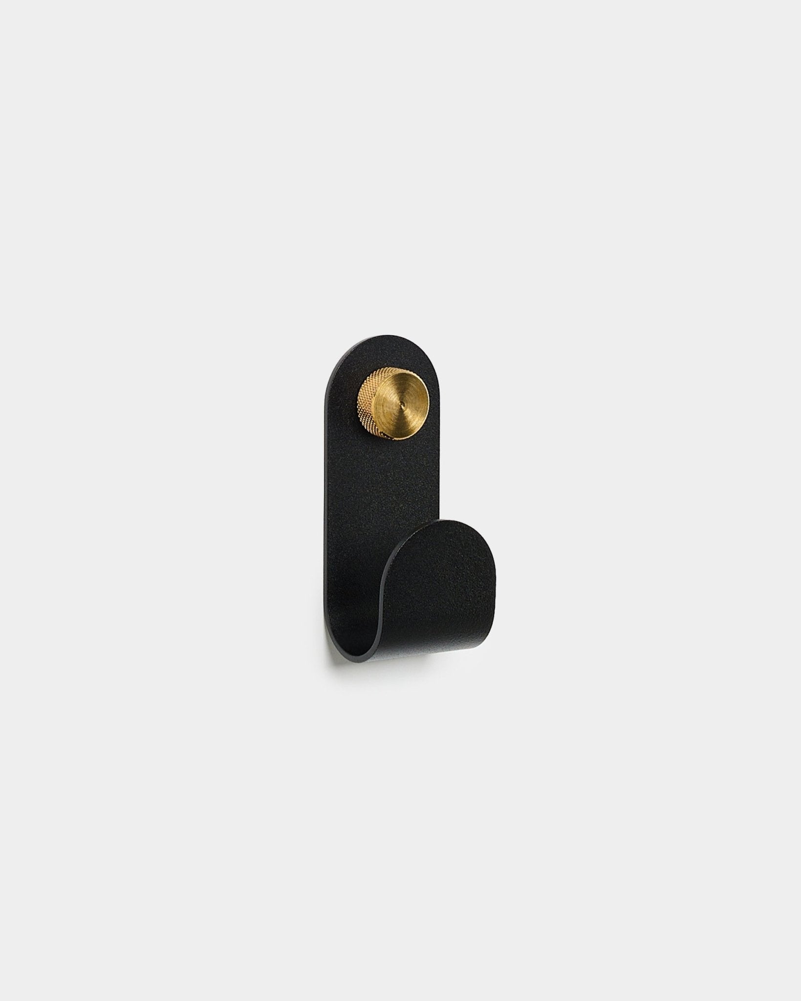 Norr Single Hanger w kolorze black od WoodUpp, o zaokrąglonej formie i z okrągłym akcentem brass, na jednolitym białym tle.
