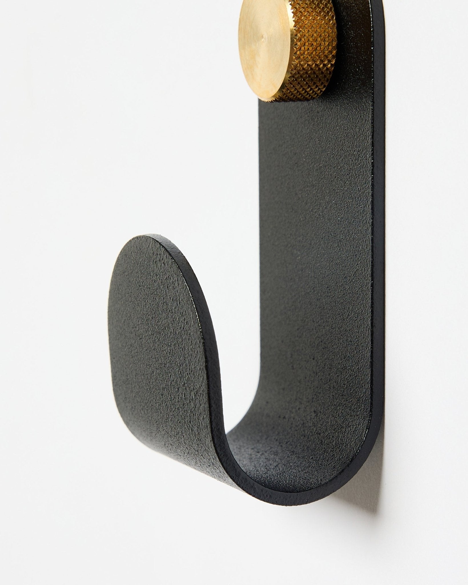 Norr Single Hanger od WoodUpp ma zakrzywione metalowe ramię w kolorze black ze złotą końcówką i został zaprojektowany jako akcesorium do paneli akustycznych na białe ściany.
