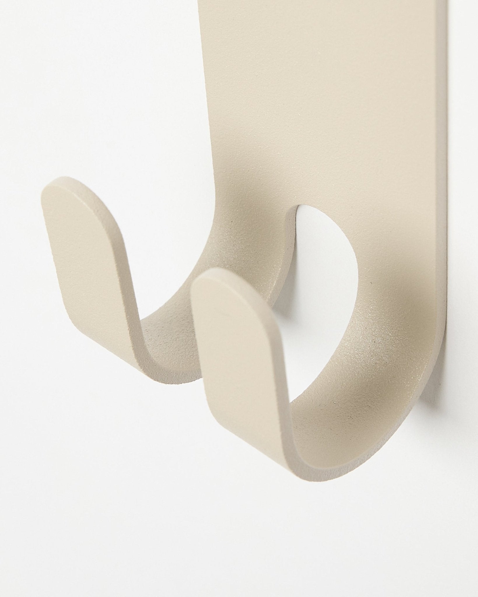 Zbliżenie na Norr Double Hanger w kolorze beige od WoodUpp, minimalistyczny metalowy haczyk na ubrania zamontowany na jasnym panelu z listew colored Panel akustyczny.