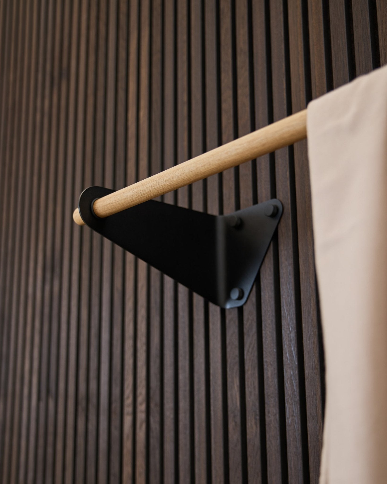 Wieszak na ubrania Linn od WoodUpp w kolorze black (115,9 cm), zamontowany na ciemnym ryflowanym Akupanel Panel akustyczny, z tekstylnym akcentem beige i wspornikiem black.