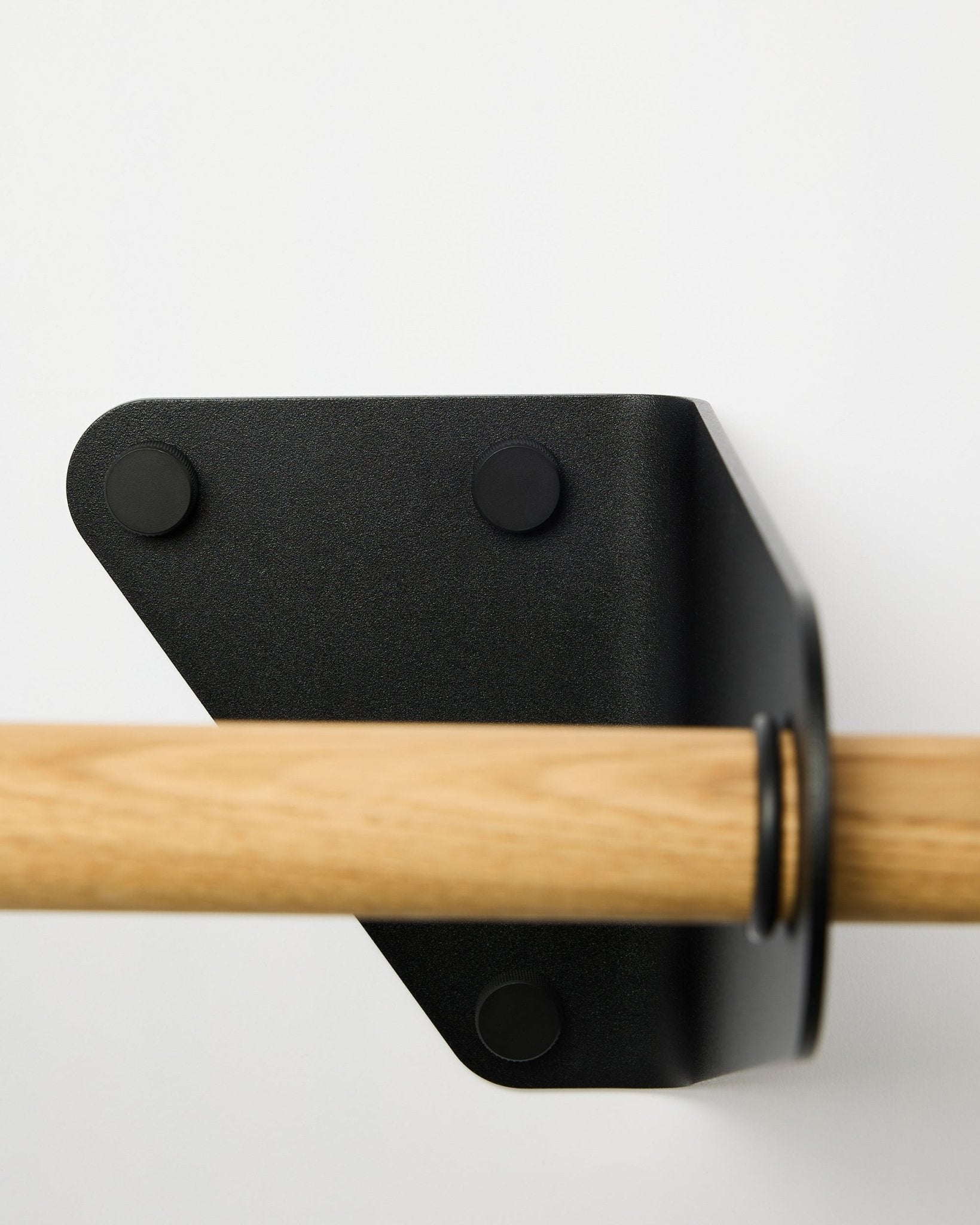 Zbliżenie na wieszak na ubrania WoodUpp Linn w kolorze black, 115,9 cm, zamontowany na białej ścianie z trójkątnym metalowym wspornikiem, pokazany jako część nordyckich akcesoriów akustycznych.