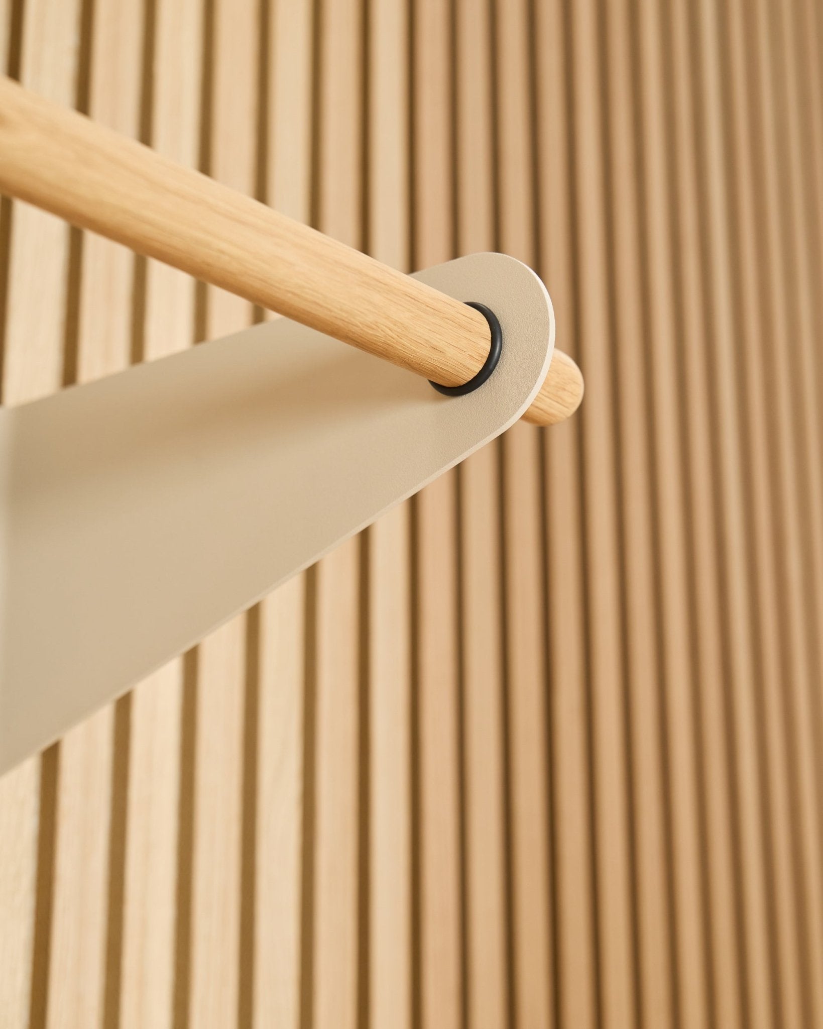 Zbliżenie na wieszak Coat Rail WoodUpp w kolorze beige (75,9 cm), zamocowany na metalowym wsporniku beige na tle teksturowanego panelu akustycznego z lamelami w kolorze Akupanel.