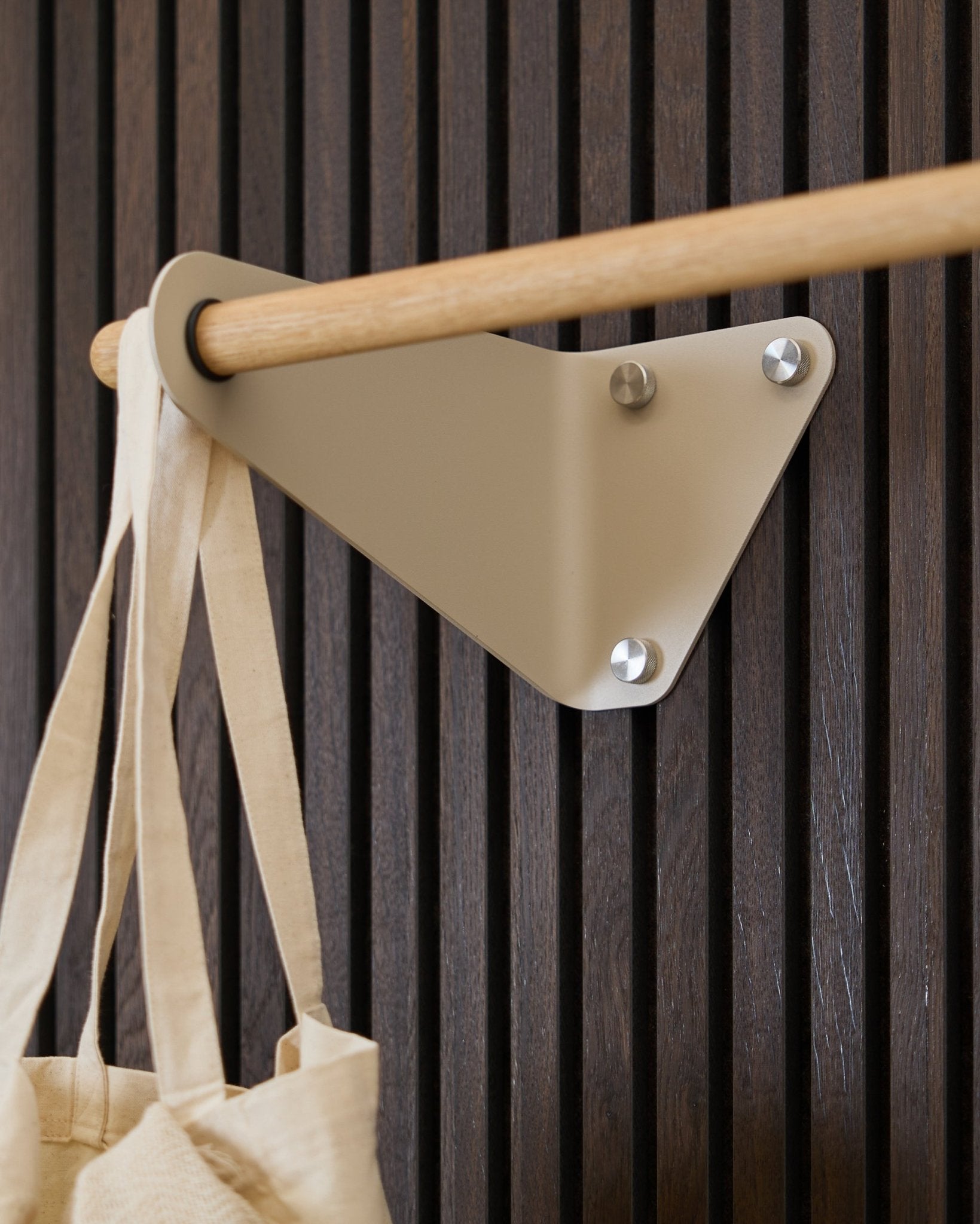 Wieszak ścienny WoodUpp Linn (115,9 cm) w kolorze Beige, zamontowany na Akupanel Panel akustyczny, z kremową torbą materiałową zawieszoną po lewej stronie.