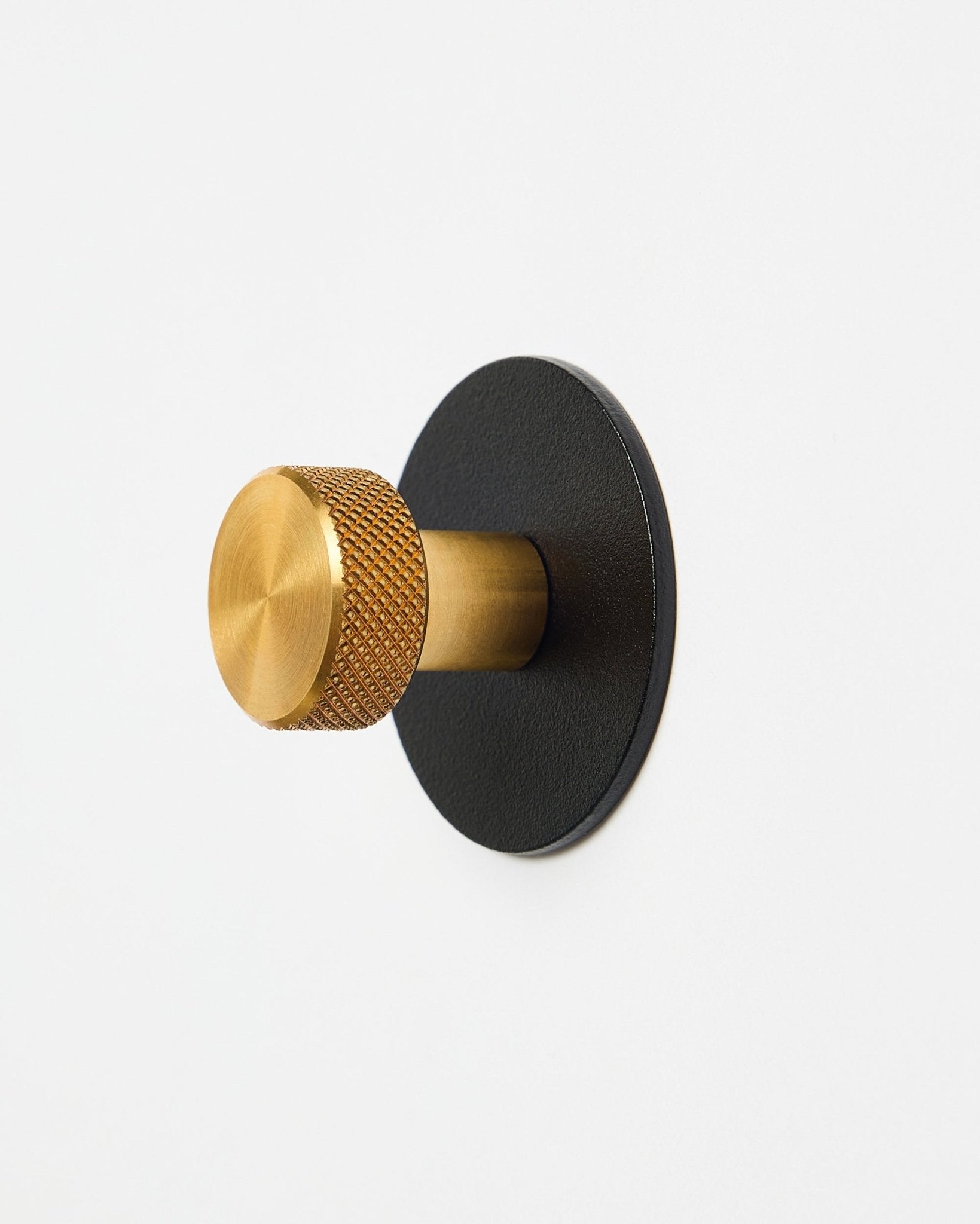Wieszak na płaszcz Norr Coat Hook X1 od WoodUpp z fakturowanym gałką brass i podstawą z malowanej proszkowo steel black, akcesorium do Akupanel, pokazany na białym tle.