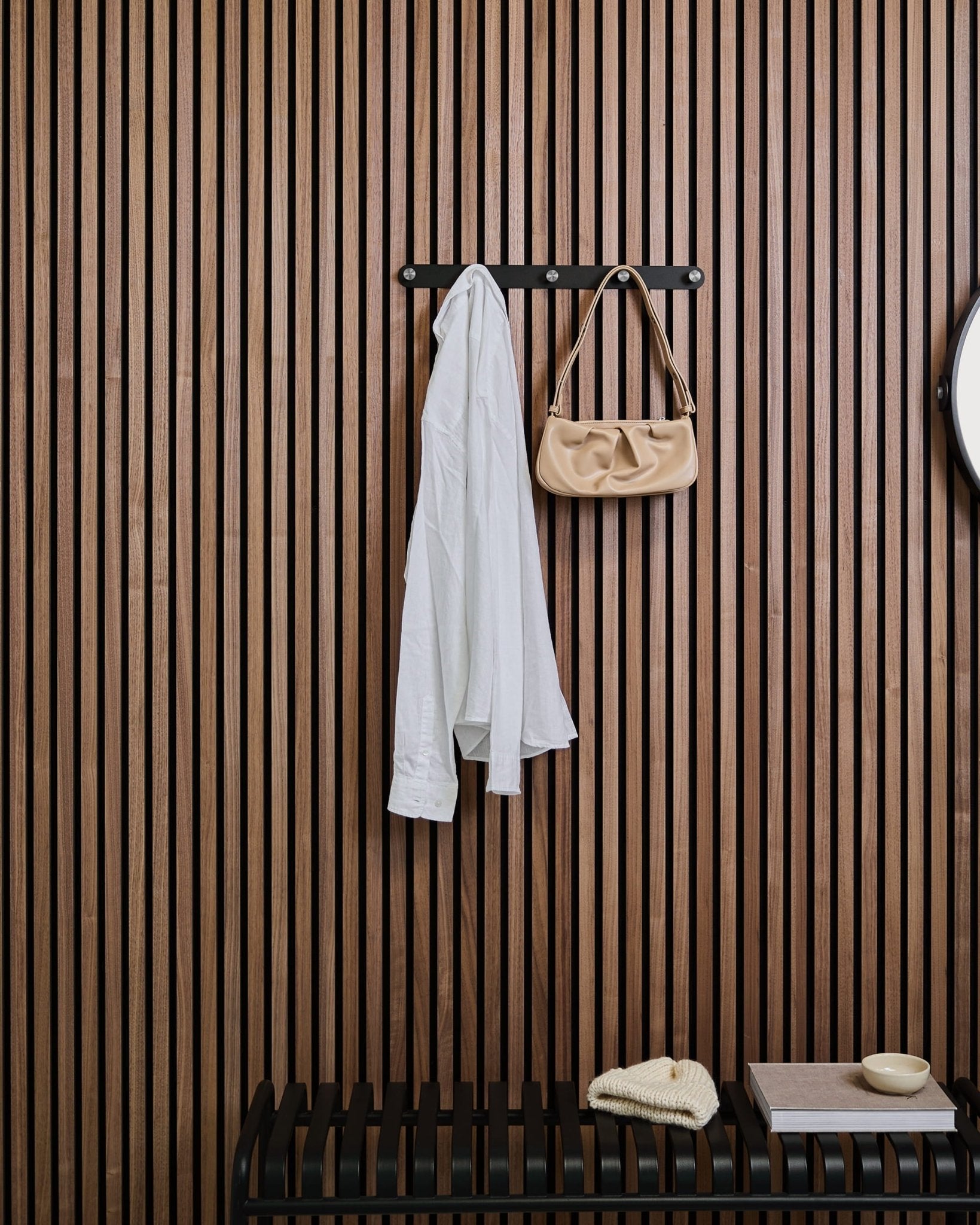 Na wieszaku WoodUpps Norr Coat Hook Rack nad ławką wiszą biała koszula i torebka beige, na tle drewnianego panelu lamelowego Akupanel z dekoracjami.