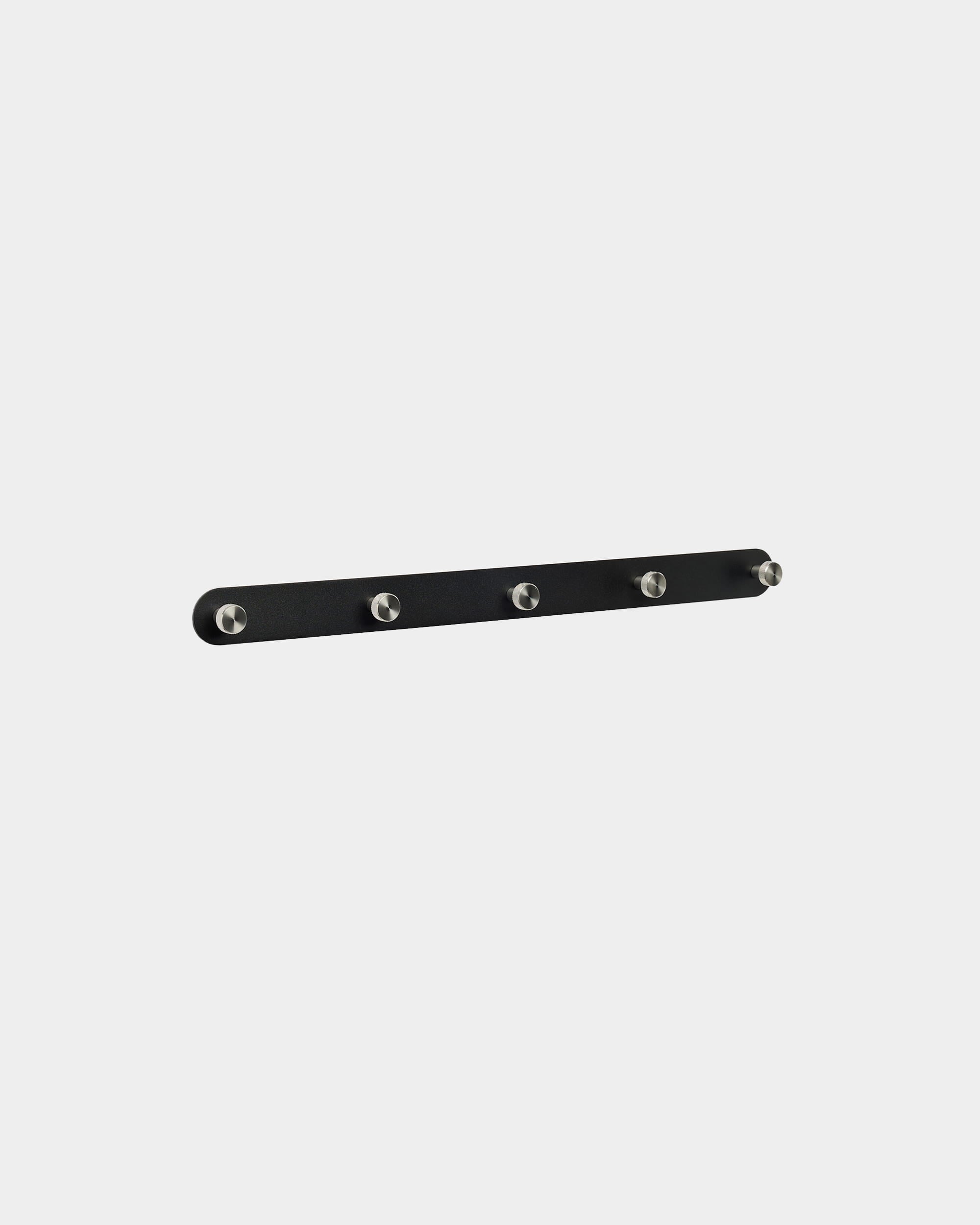 Wieszak ścienny WoodUpp Norr X5 w kolorze black i ze stali nierdzewnej, z pięcioma równomiernie rozmieszczonymi haczykami, zamontowany na jednolitym białym tle. Minimalistyczny design w stylu nordyckim.