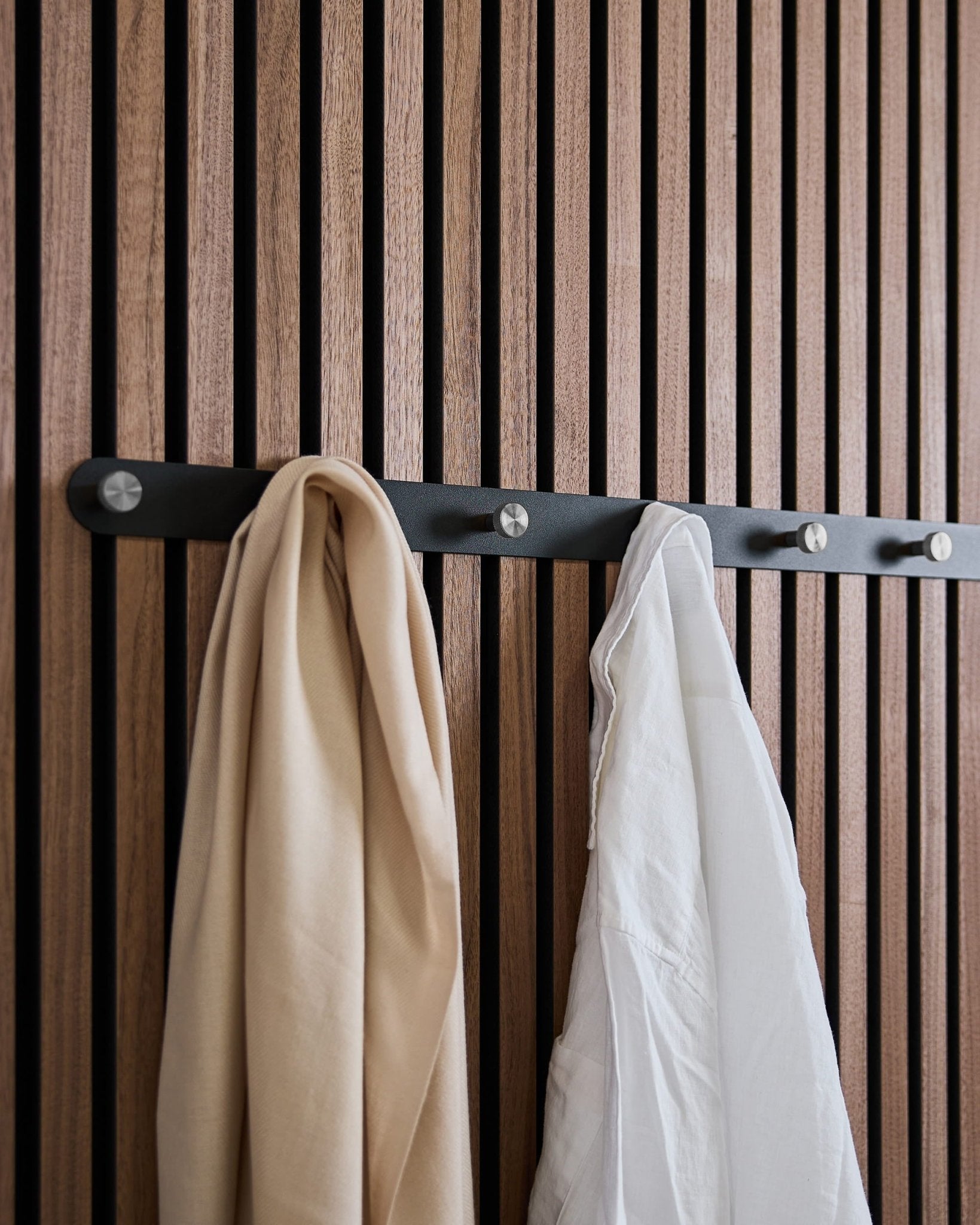beige szalik i biała koszula wiszą na wieszaku ściennym WoodUpp Norr X7 Black/Stainless Steel, zamontowanym na nordyckim panelu akustycznym z drewnianymi lamelami.