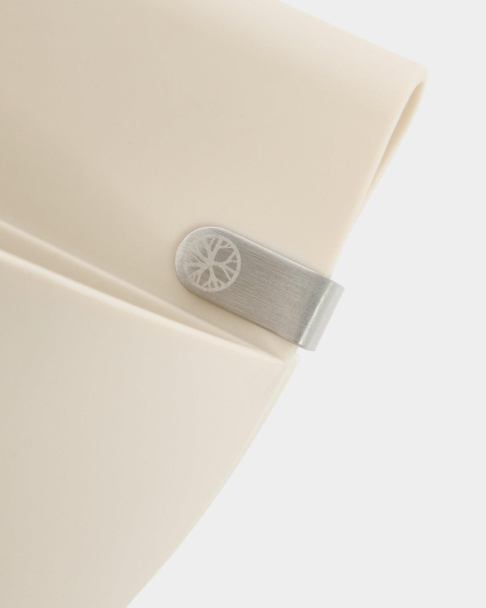 Zbliżenie na panel WoodUpp Gro | Soft Pocket / BM2 (4 l) w jasnym odcieniu beige, z metalowym klipsem i grawerowanym detalem w kształcie koła, na jednolitym białym tle.