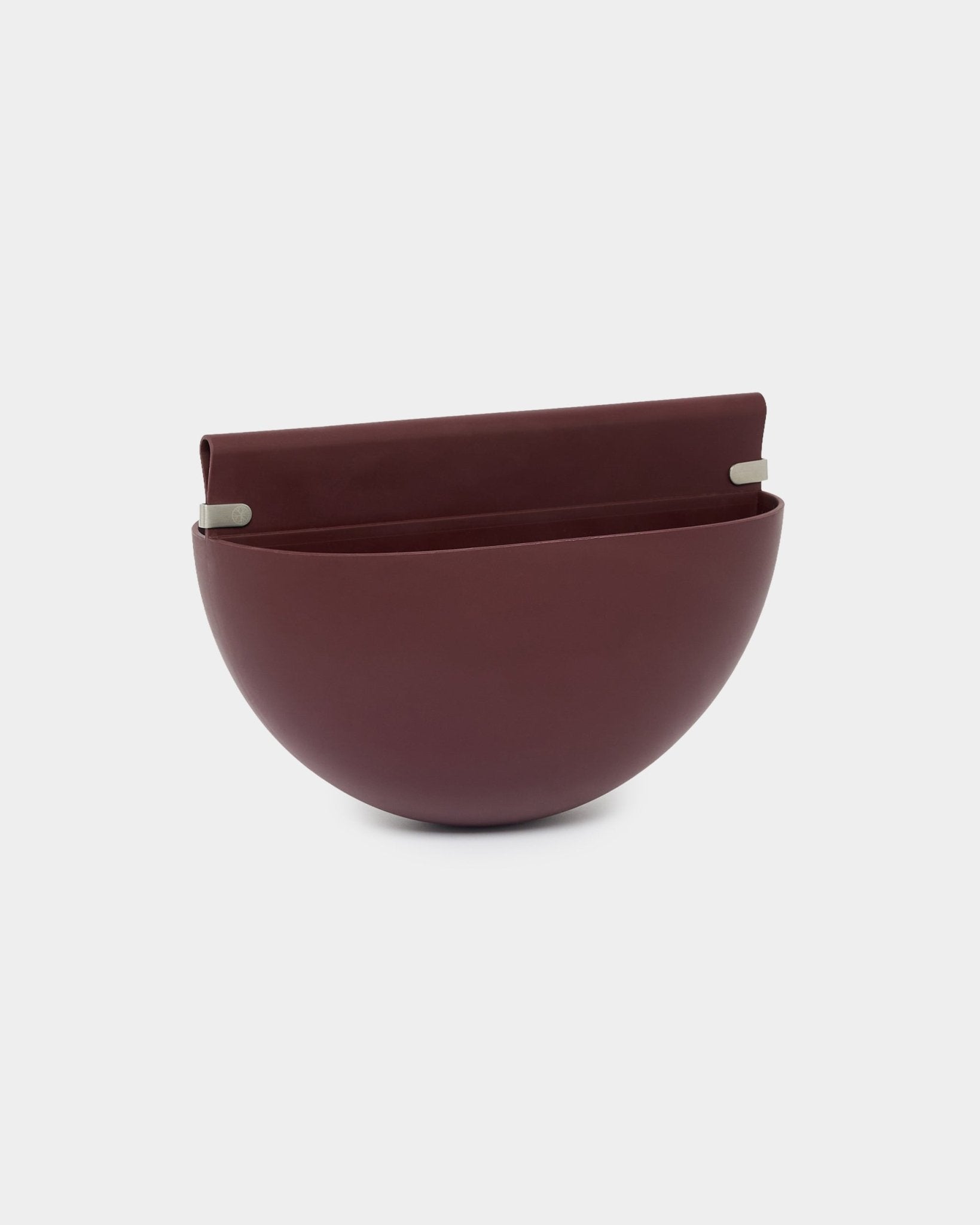 Doniczka WoodUpp Gro Soft Pocket / BM2 w kolorze Ox Red, o pojemności 4 l, ma formę półkuli, płaski tył i dwa metalowe uchwyty do montażu na panelach akustycznych.
