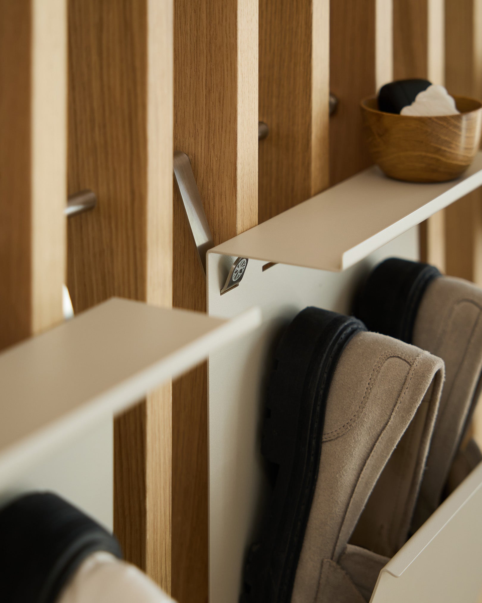 Minimalistyczny stojak na buty WoodUpp w kolorze beige, z malowanego proszkowo steel, zamontowany na nordyckim panelu listwowym Panel akustyczny, a nad nim ustawiona miseczka small na klucze.